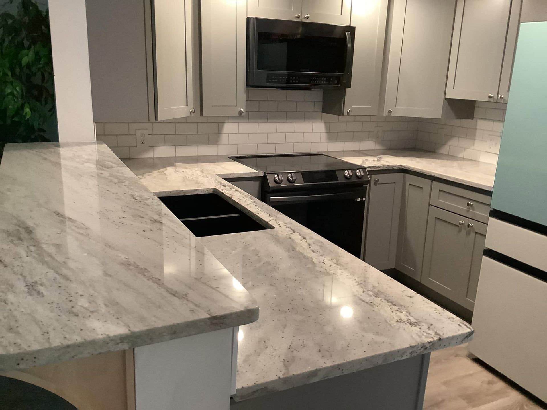 Modern kitchen with gray cabinets, marble countertops, black stove, and white appliances.