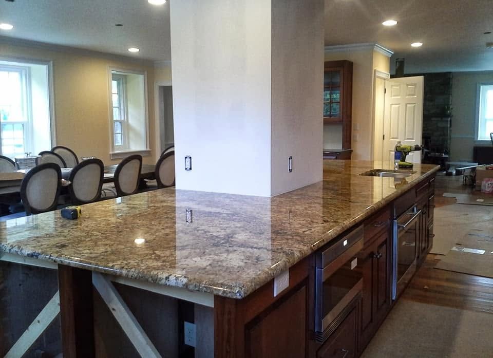 Spacious kitchen with large granite island, dark wood cabinets, and adjoining dining area and hallway.