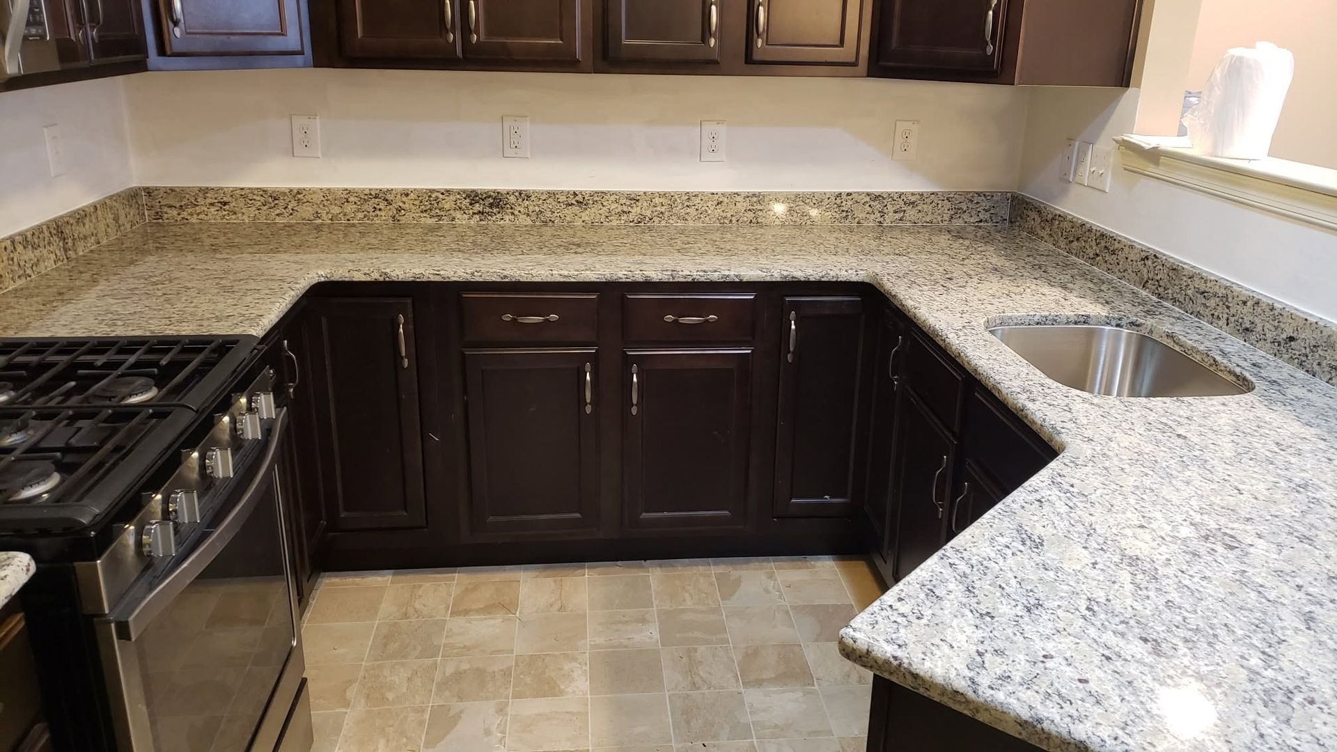 Kitchen with dark cabinets, light granite countertops, stove, sink, and tiled floor