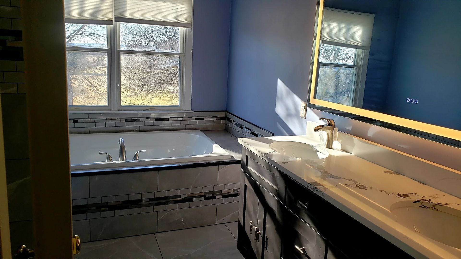 Bright bathroom under renovation with blue walls, window, sink, and cabinet pieces on the floor.