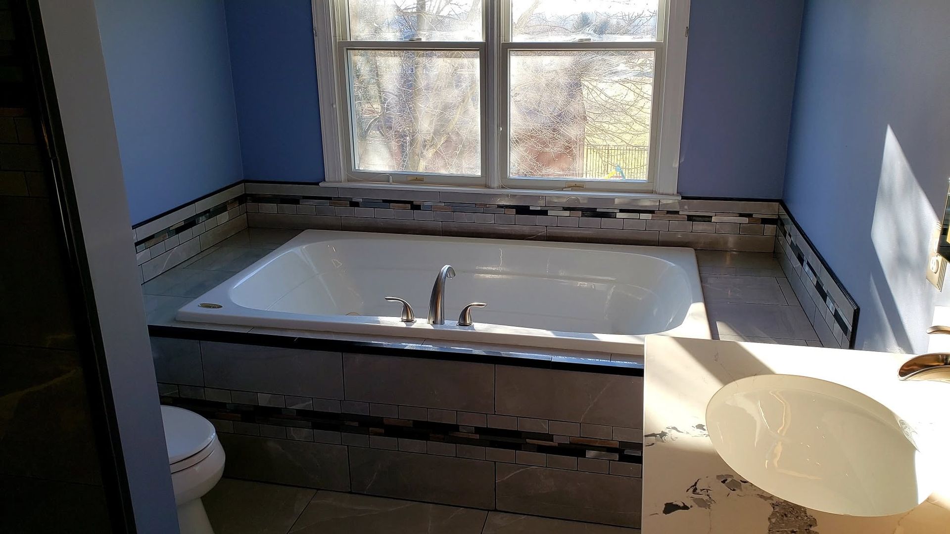 Bathroom with a white tub beneath a window and a bucket in the foreground; unfinished wall around the tub.
