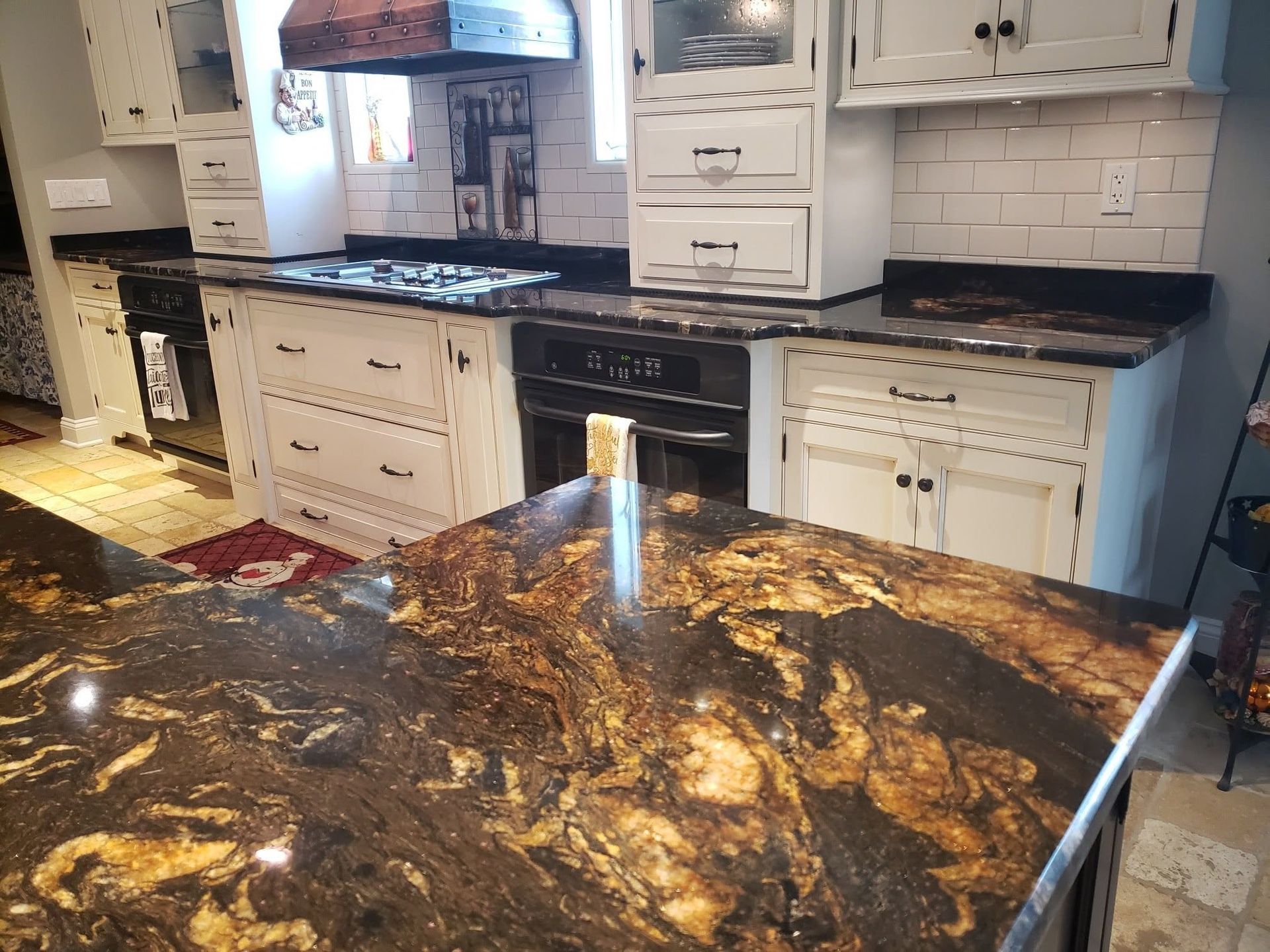 Granite kitchen island with dark, marbled countertop in front of white cabinets and stove.