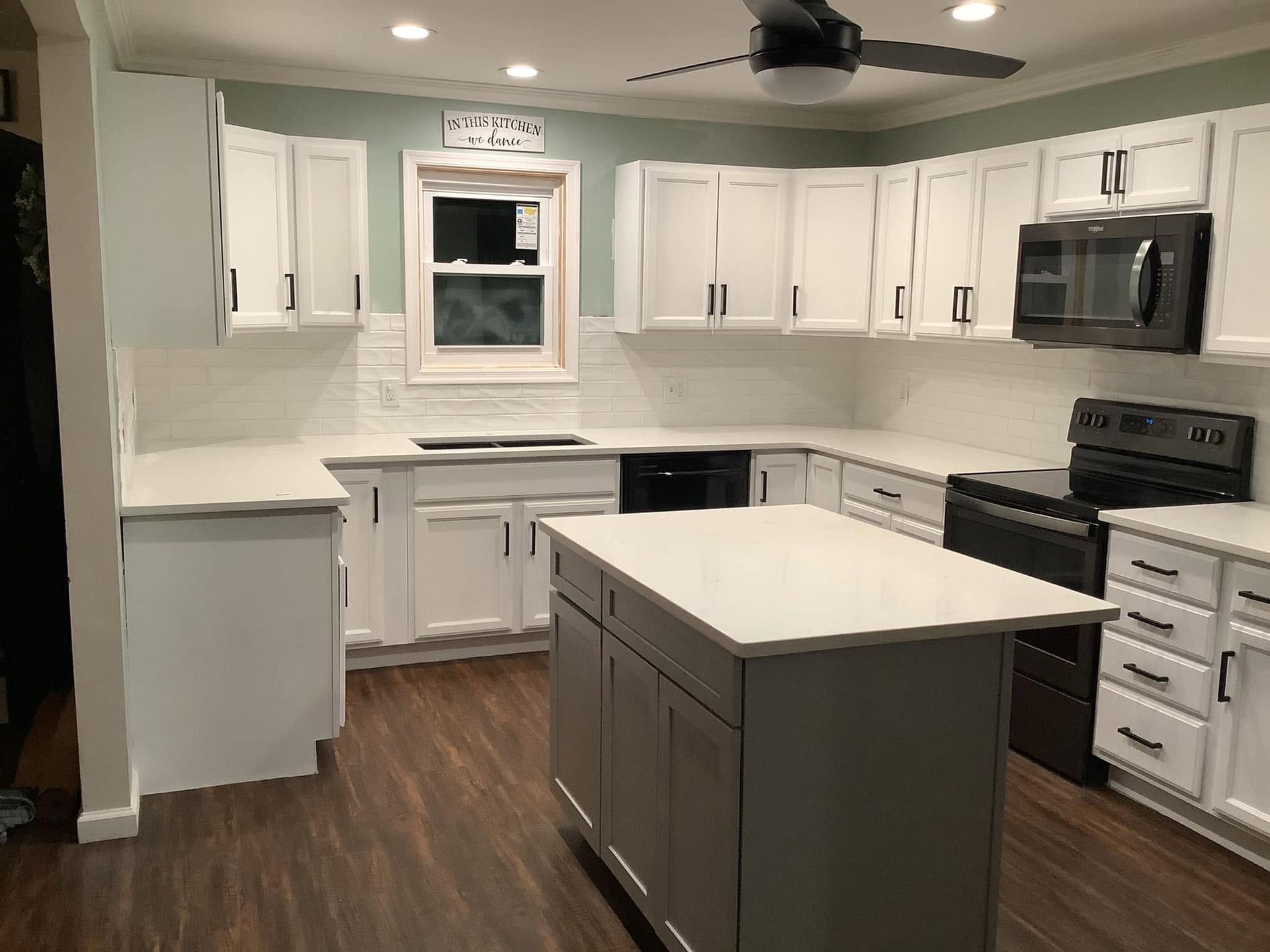 Modern kitchen with white cabinets, stainless appliances, dark island, and wood flooring