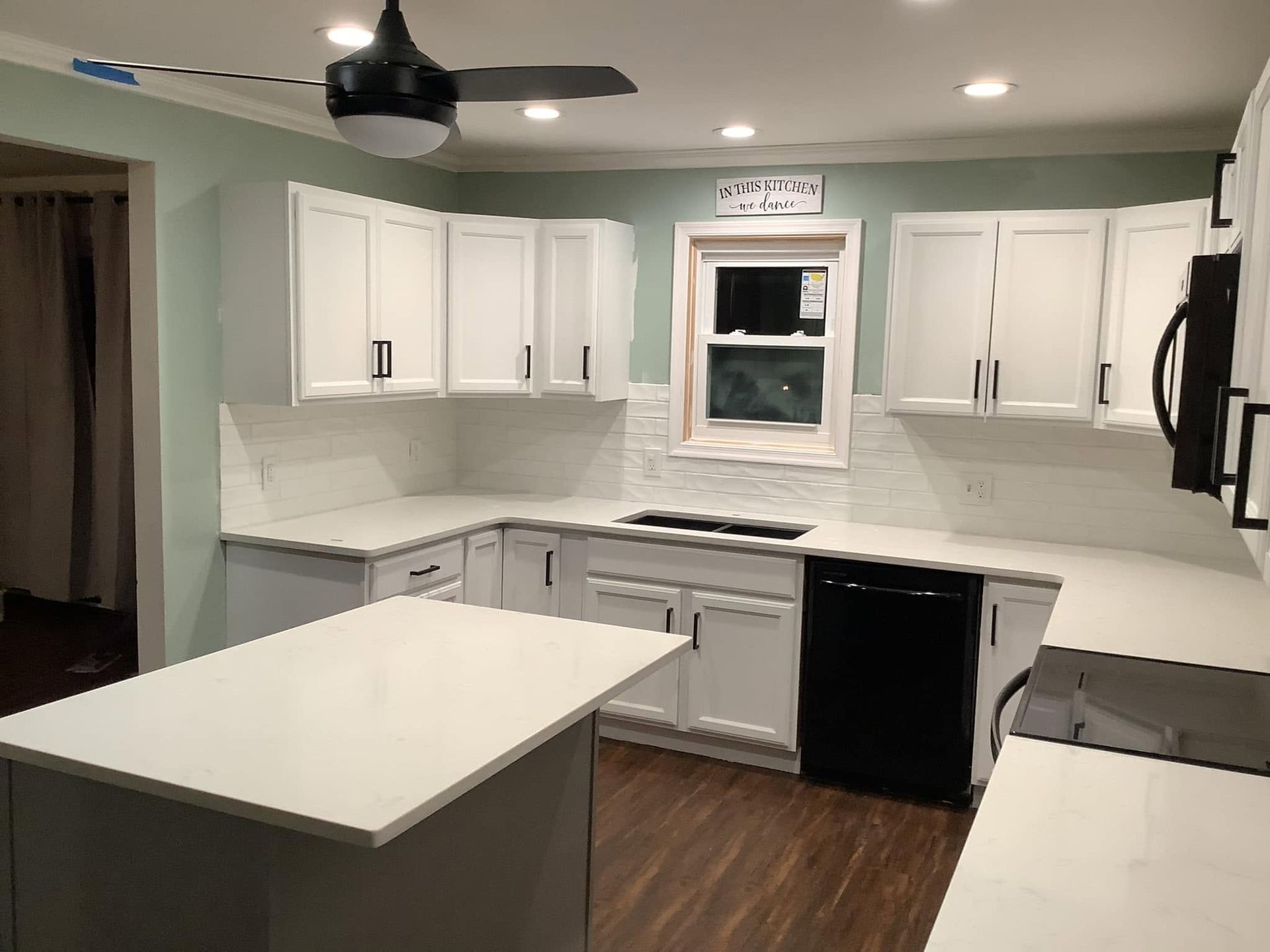 Bright white kitchen with island, white cabinets, dark countertops, and wood floor.