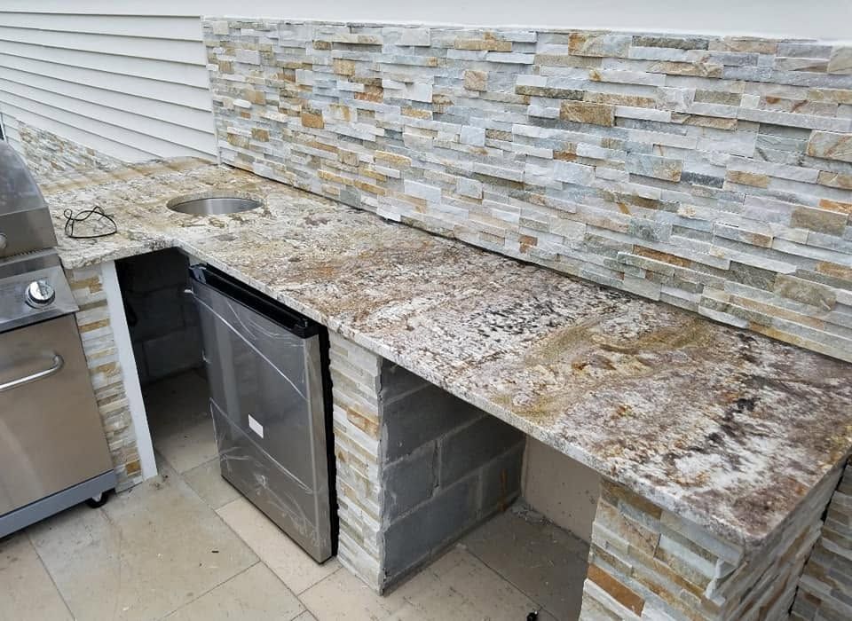 Outdoor stone kitchen counter with built-in grill and cabinet beneath a stone backsplash header