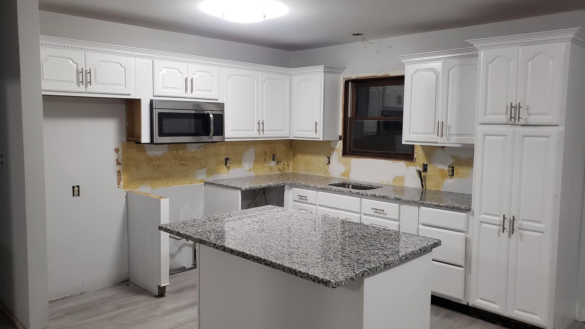 Bright white kitchen with granite island, white cabinets, stainless appliances, and yellow backsplash