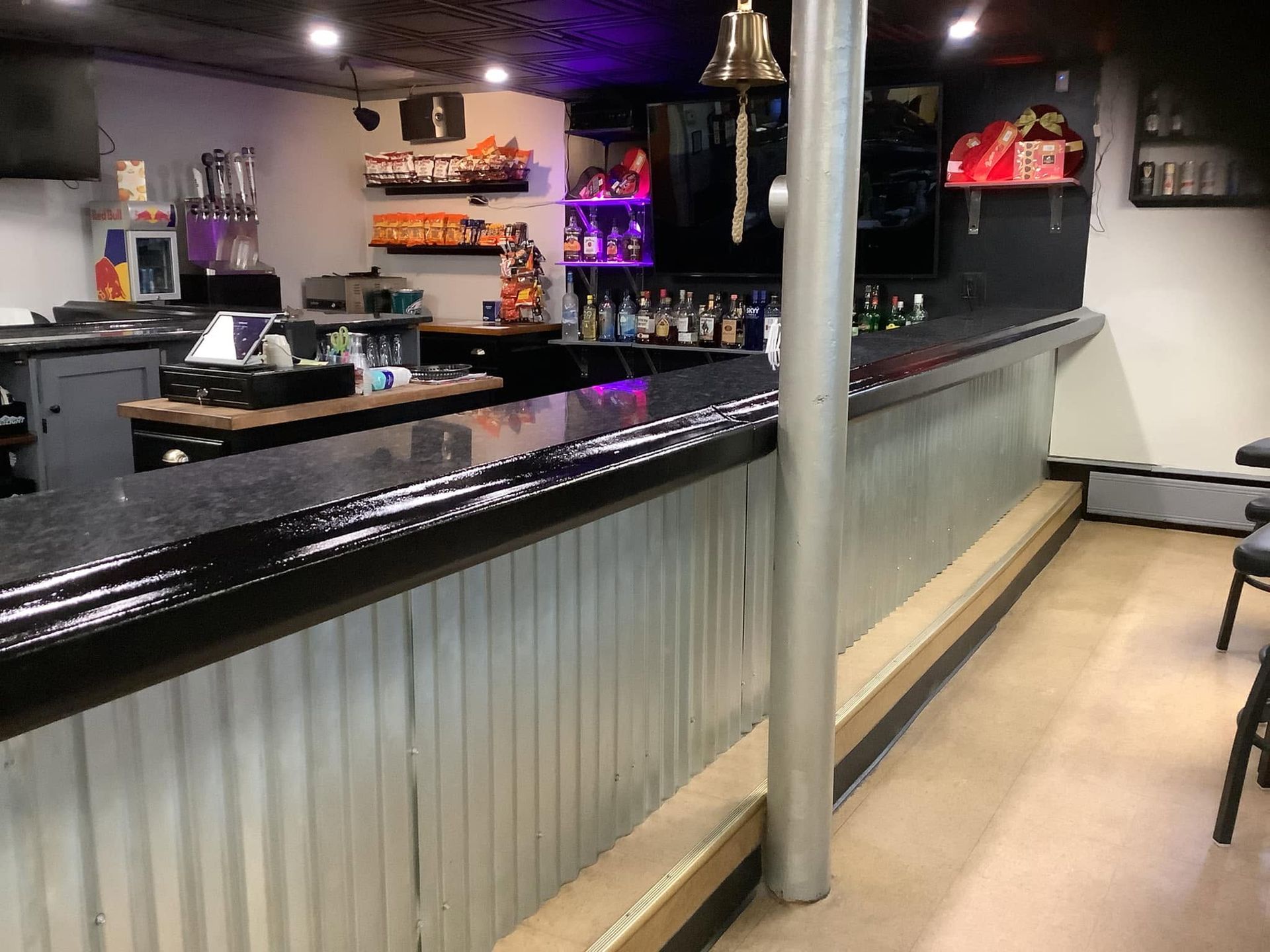 Empty bar interior with black countertop, metal paneling, and bottles on shelves under dim lighting