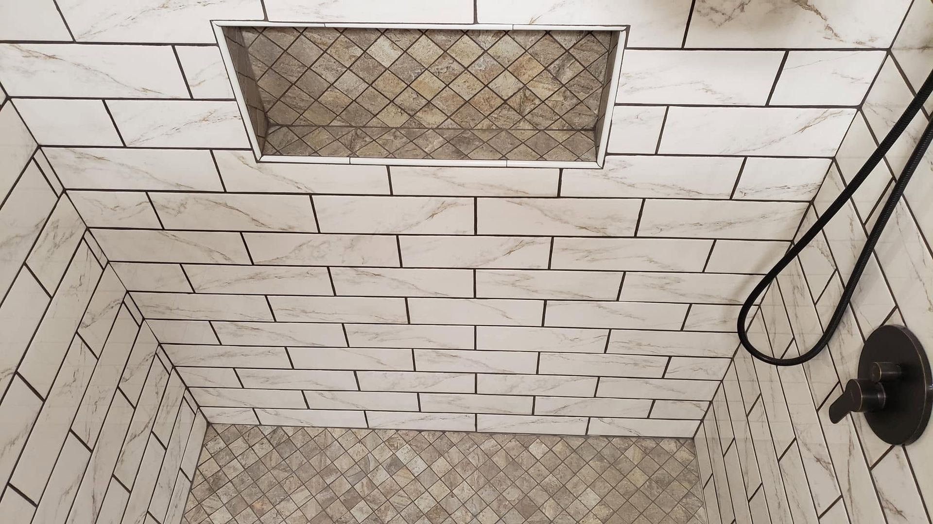 White subway-tile shower corner with metal drain covers and a black shower fixture on the right.