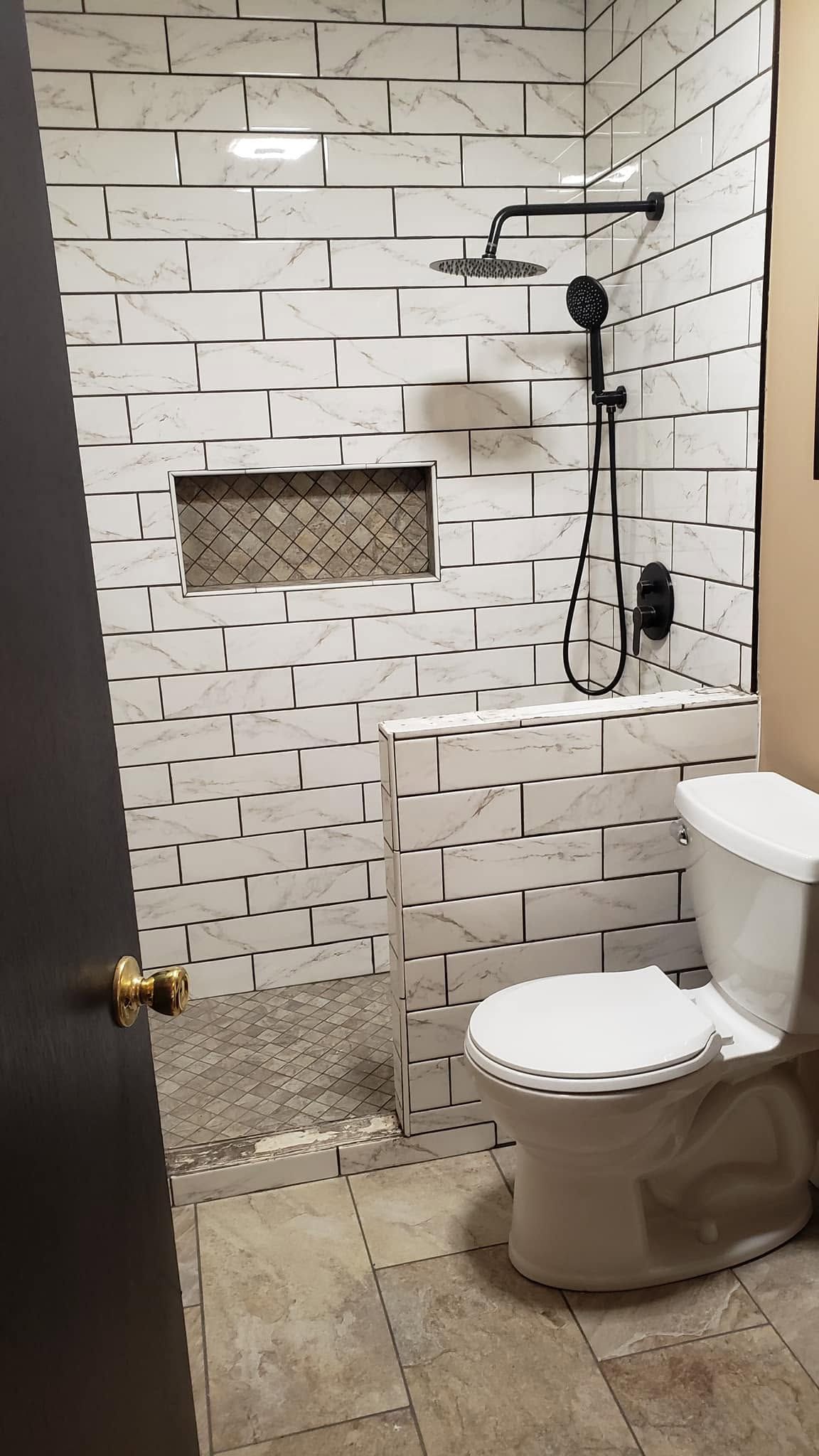 Small tiled bathroom with shower, toilet, and a wall niche; a damaged section is visible in the wall.