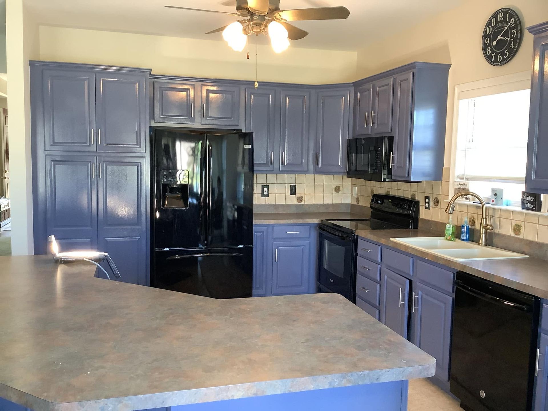 Kitchen with blue cabinets, black appliances, and a large gray island countertop