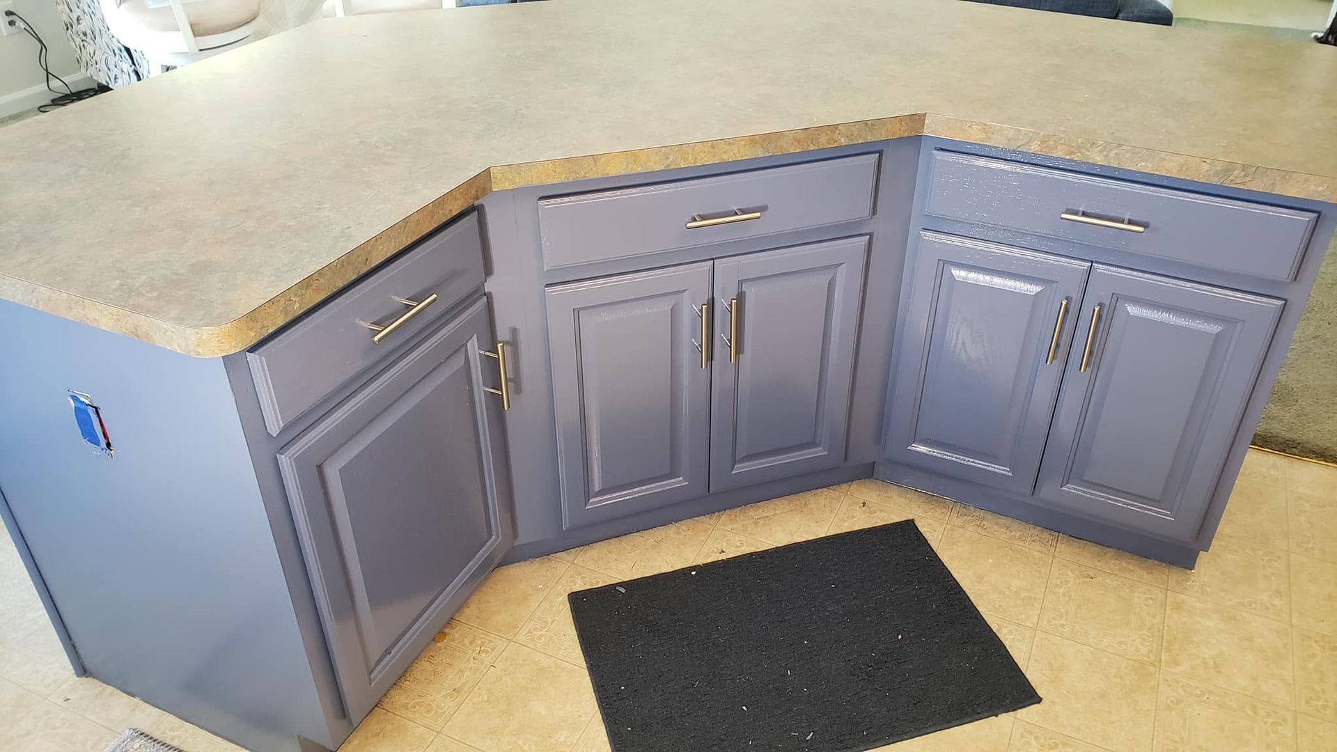 Gray kitchen cabinets with a beige countertop and black floor mat in a corner layout