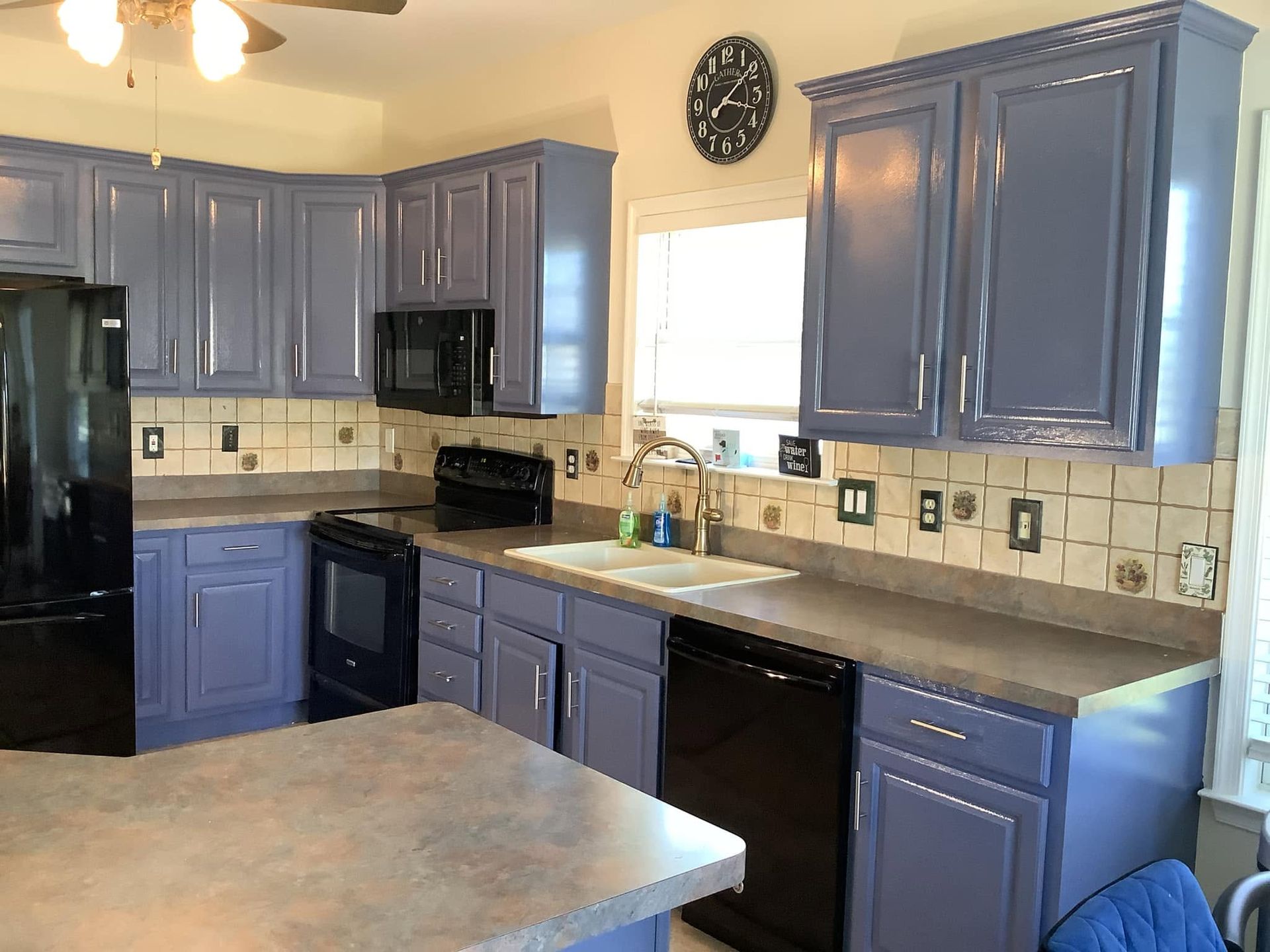 Blue kitchen with black appliances, beige tile backsplash, and a central island under a wall clock