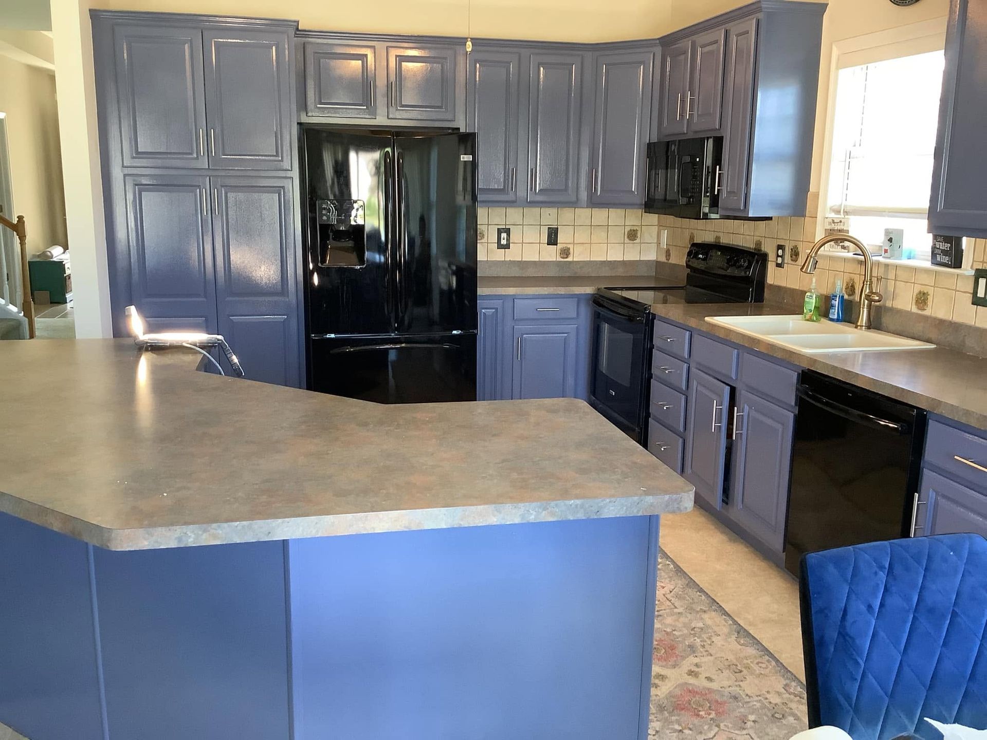 Blue kitchen with black appliances, light countertops, and a large island.