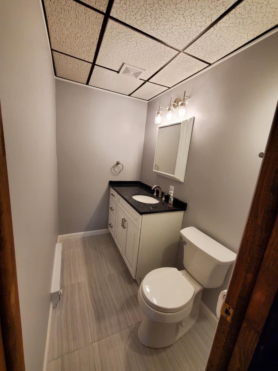Small bathroom with toilet, vanity sink, mirror, and gray tile floor.
