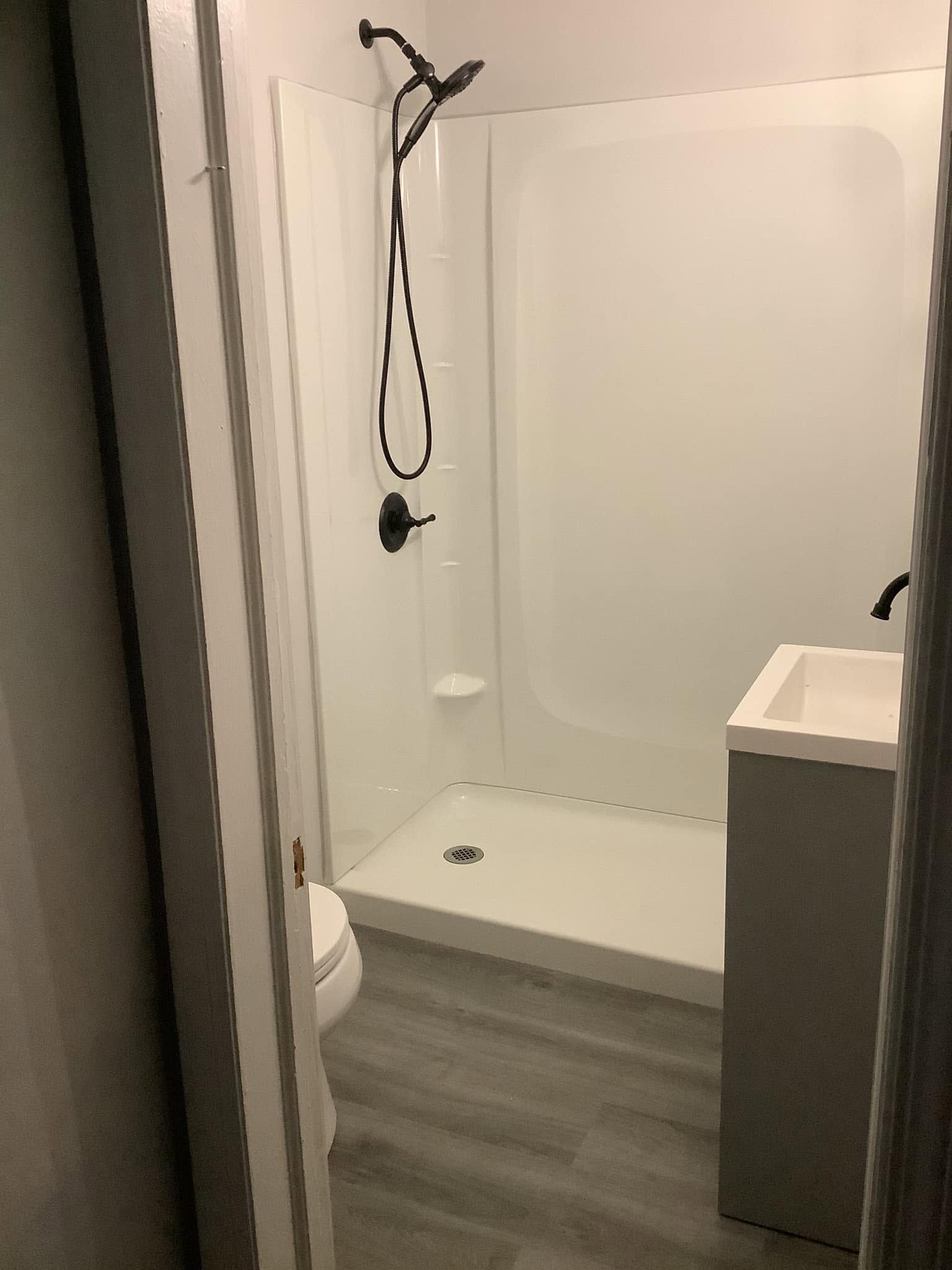 Small bathroom with a walk-in shower, wall-mounted showerhead, toilet, and gray floor.