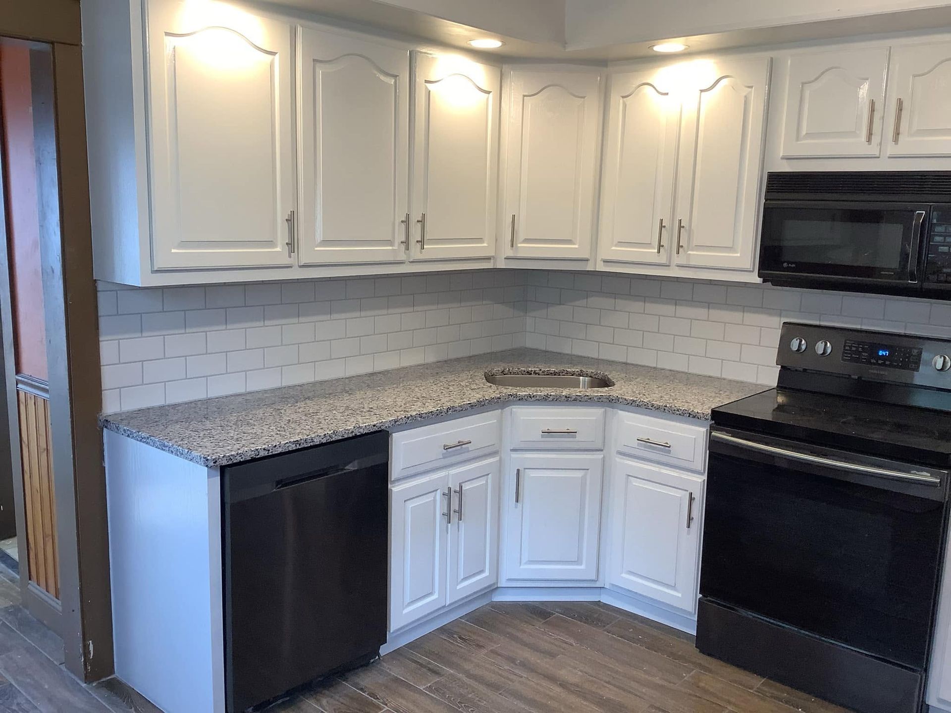 White corner kitchen with black appliances and speckled granite countertops