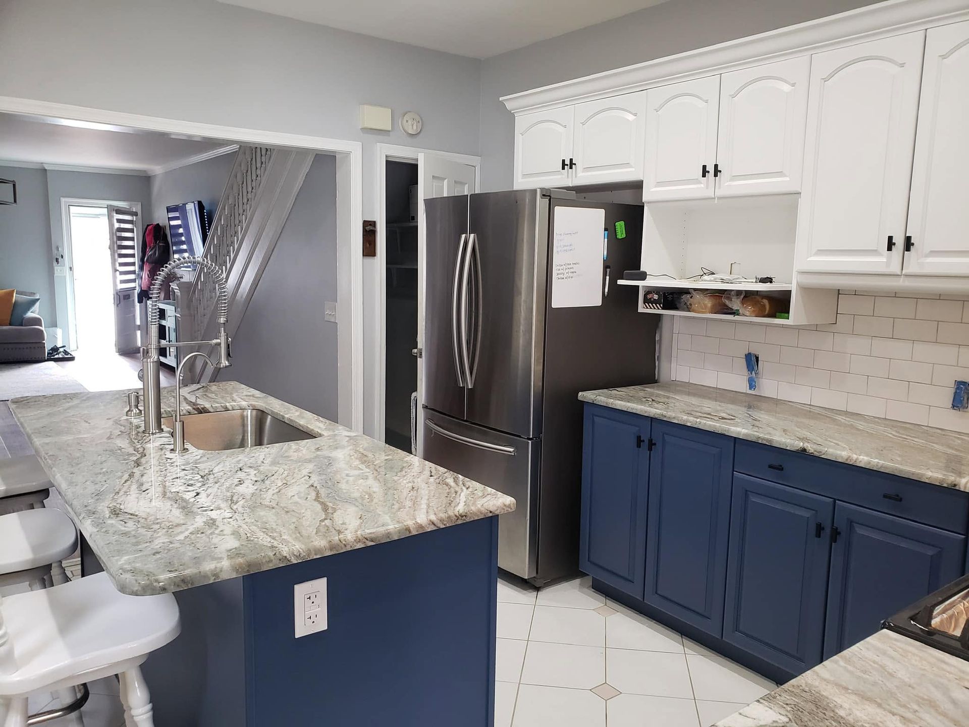 Modern kitchen with blue cabinets, granite island, stainless fridge, and white tile floor