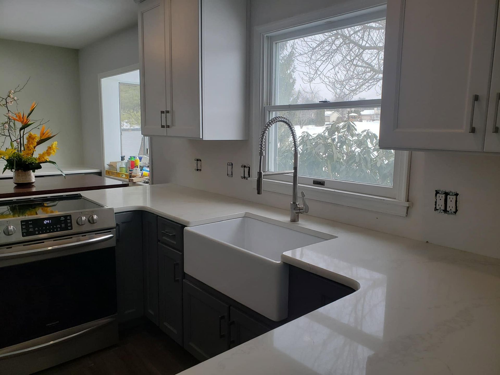 Modern kitchen with white cabinets, dark lower cabinets, stove, sink, and large window over the counter.
