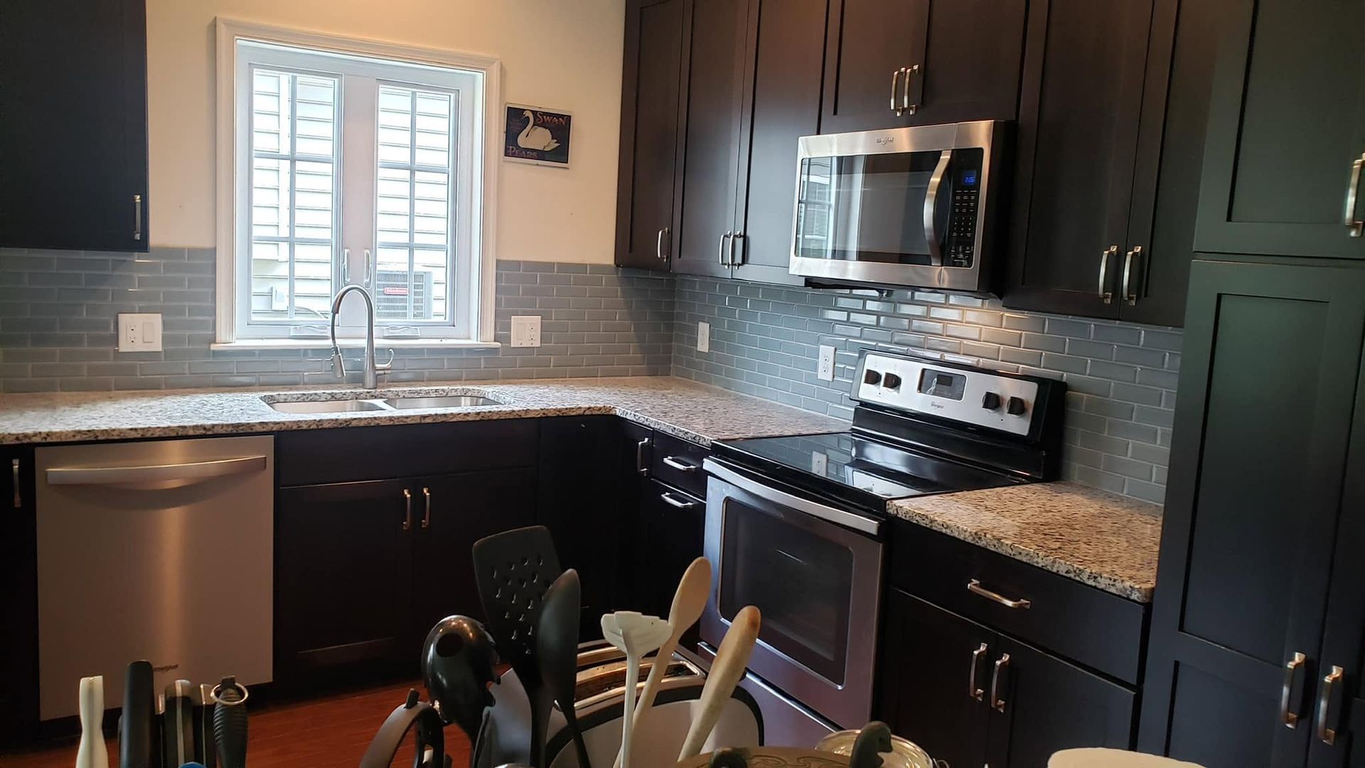 Modern kitchen with dark cabinets, granite countertops, stainless steel appliances, and a window over the sink