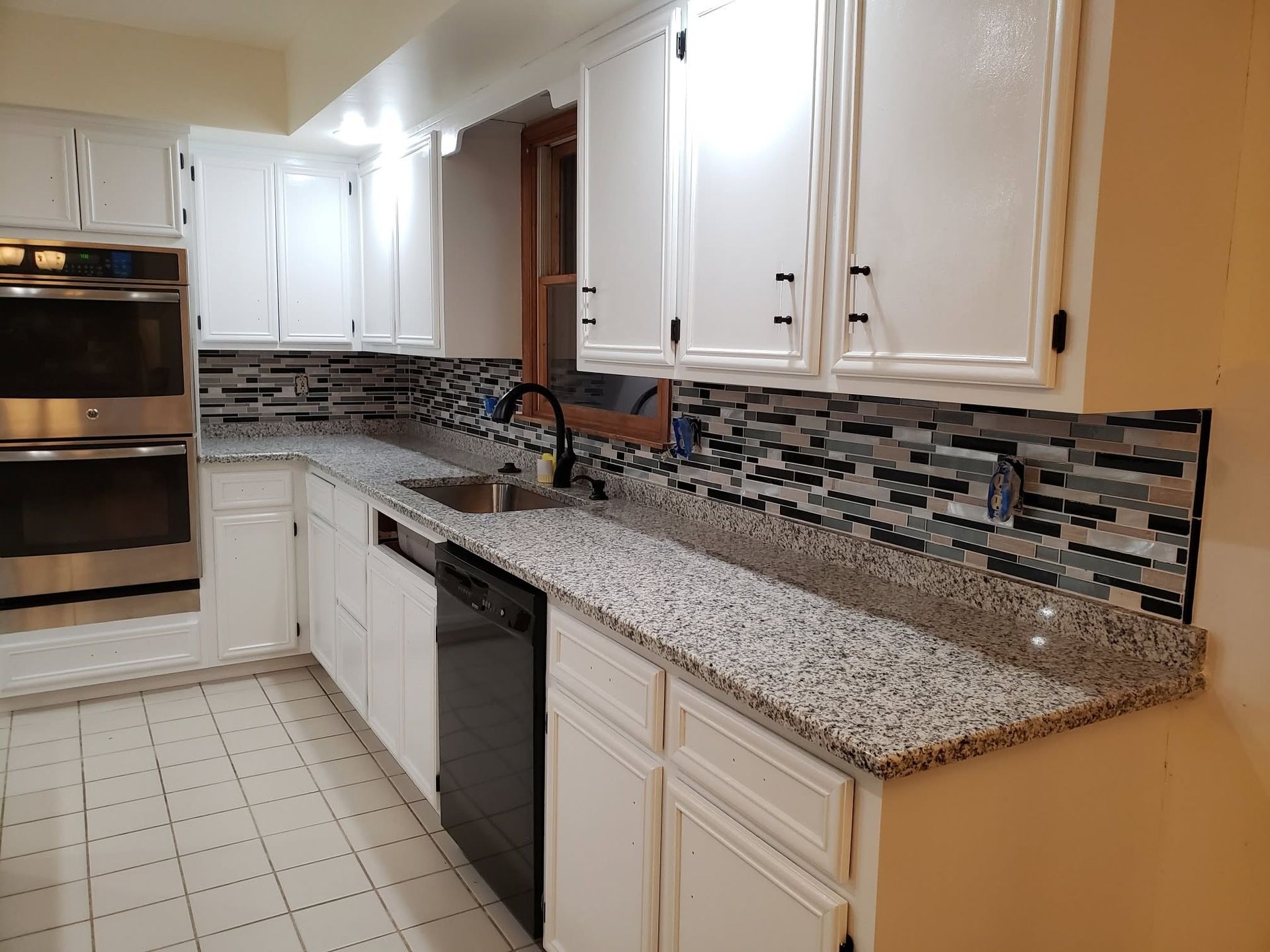 Modern kitchen with white cabinets, granite countertops, mosaic backsplash, and built-in stainless steel oven.
