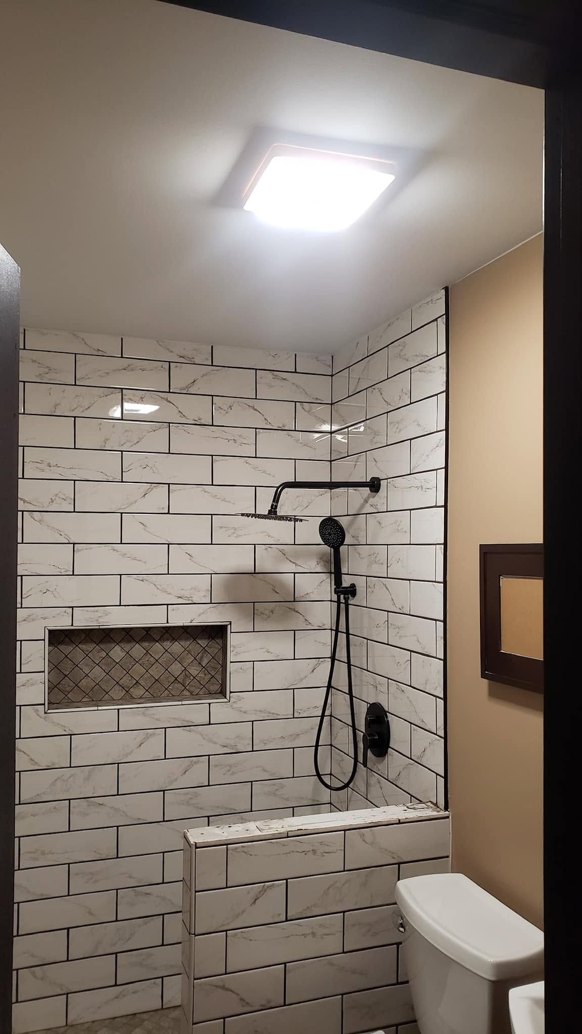 Small bathroom with white brick-style tile, a walk-in shower, vanity, and toilet under a bright ceiling light.