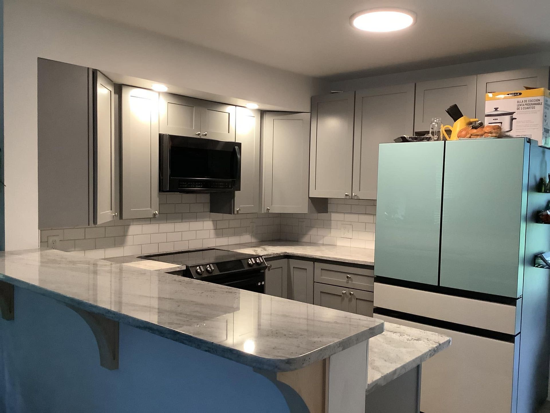 Modern kitchen with gray cabinets, marble counters, stainless appliances, and a light blue refrigerator