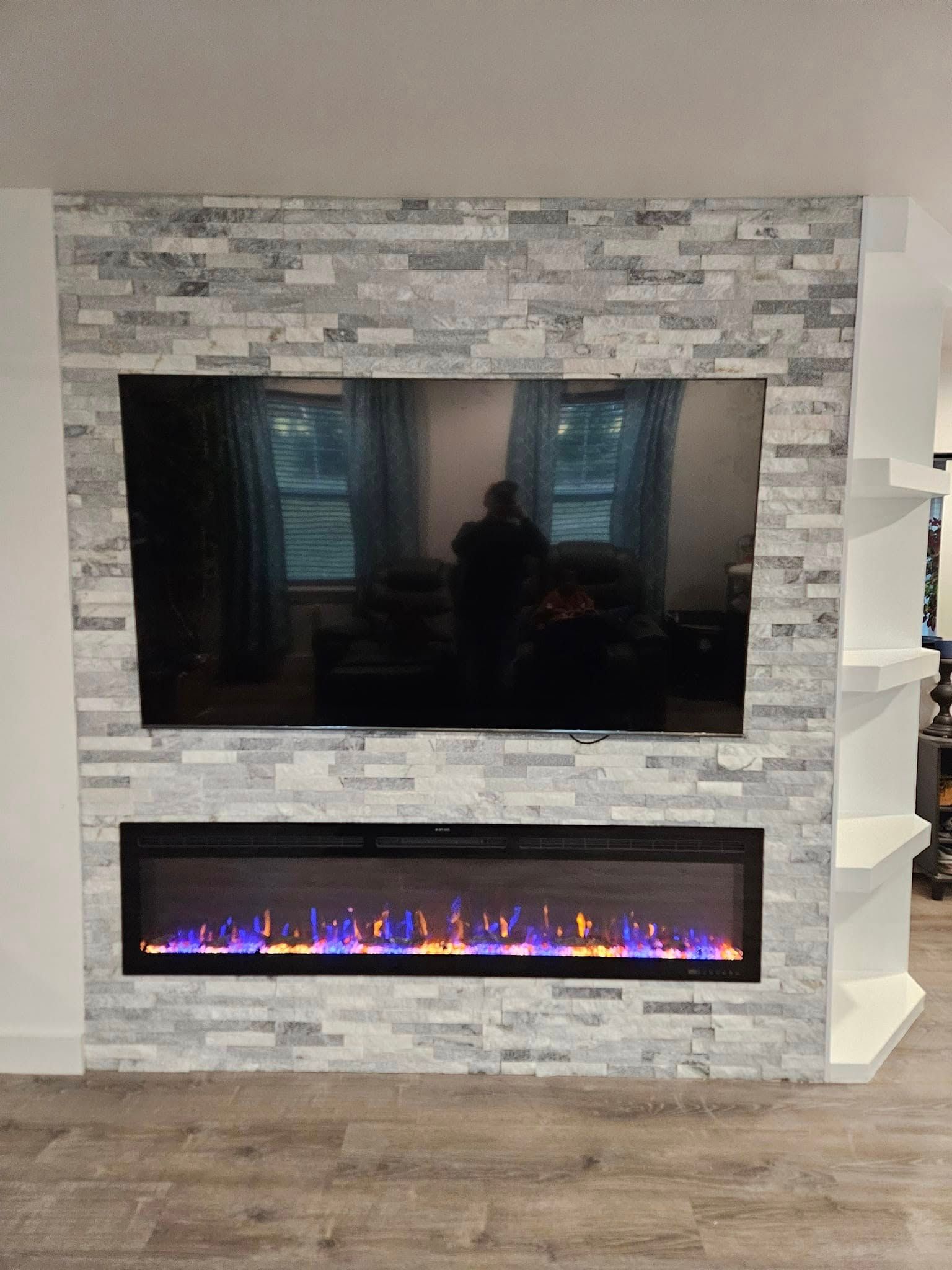 Modern electric fireplace with stone surround and large TV above, flame effect lit below.