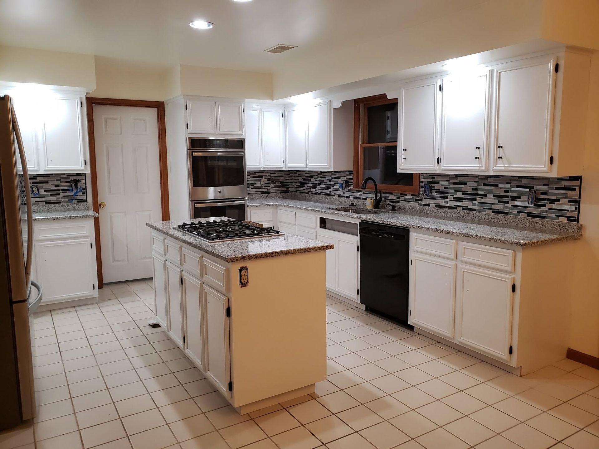 Bright kitchen with white cabinets, tiled floor, black appliances, and a central island.