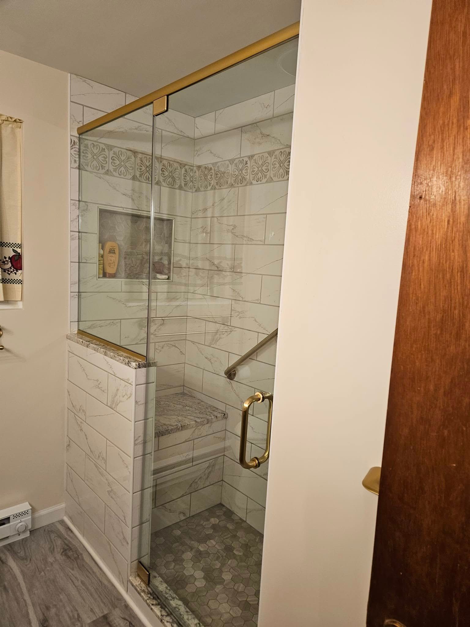 Glass shower stall with white tile walls and a brass-framed door in a bathroom