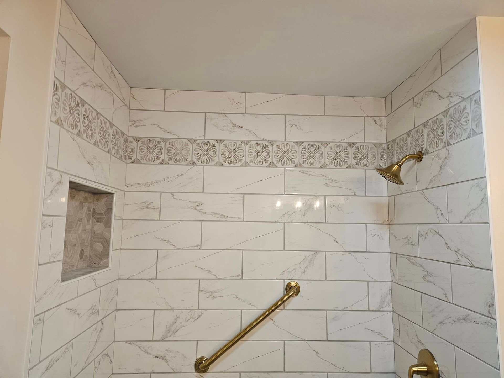 White tiled shower stall with brass grab bar and fixtures, and a built-in niche on the left