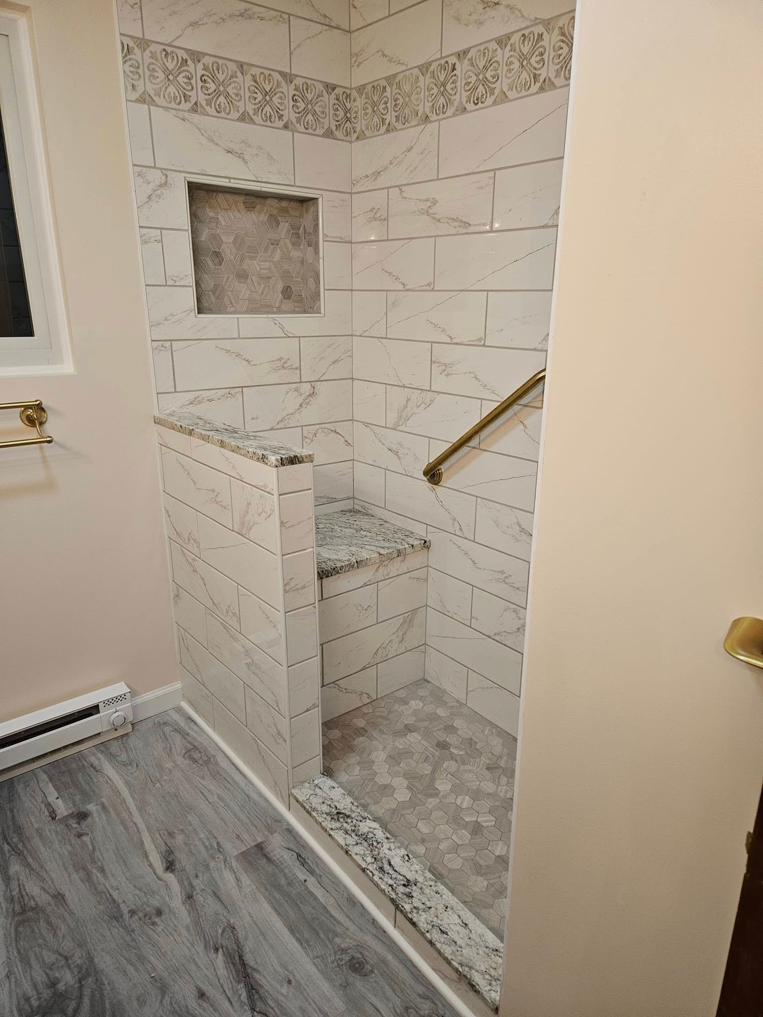 Small tiled shower stall with a built-in bench, grab bar, and recessed niche in a bathroom.