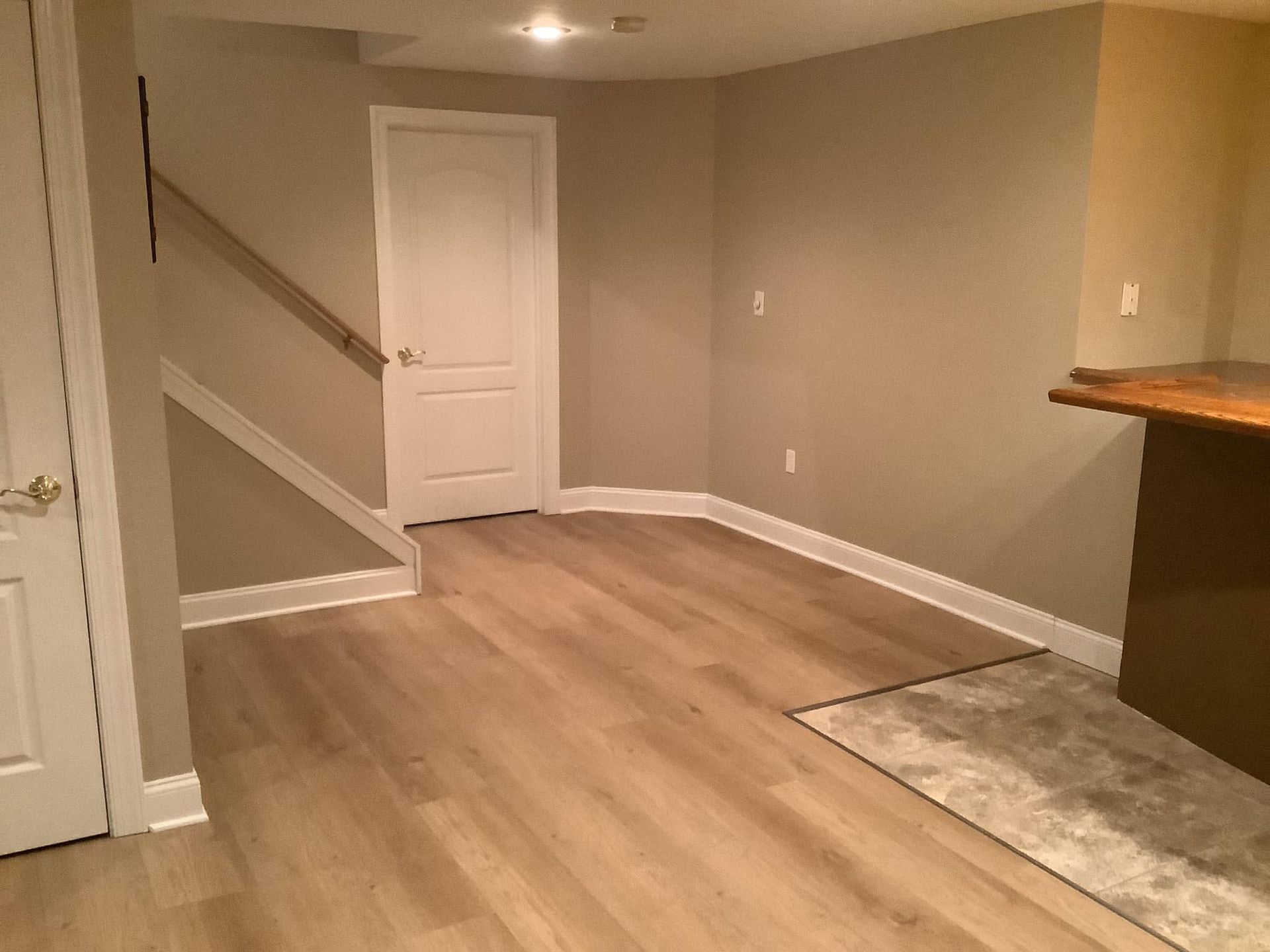 Empty beige room with wood-look flooring, white door, and a staircase on the left