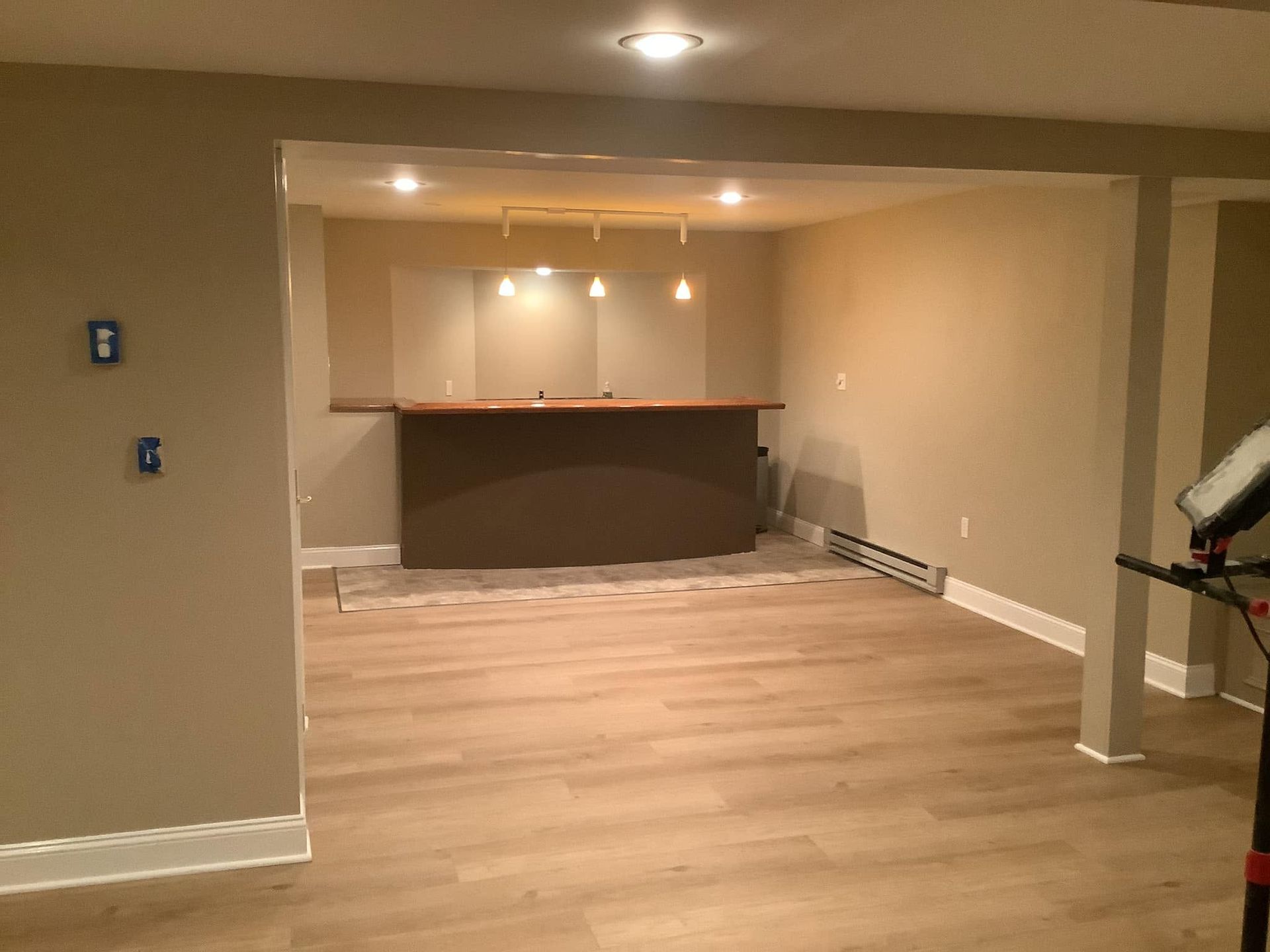 Empty basement rec room with light wood floor, recessed lights, and a small bar counter at the back