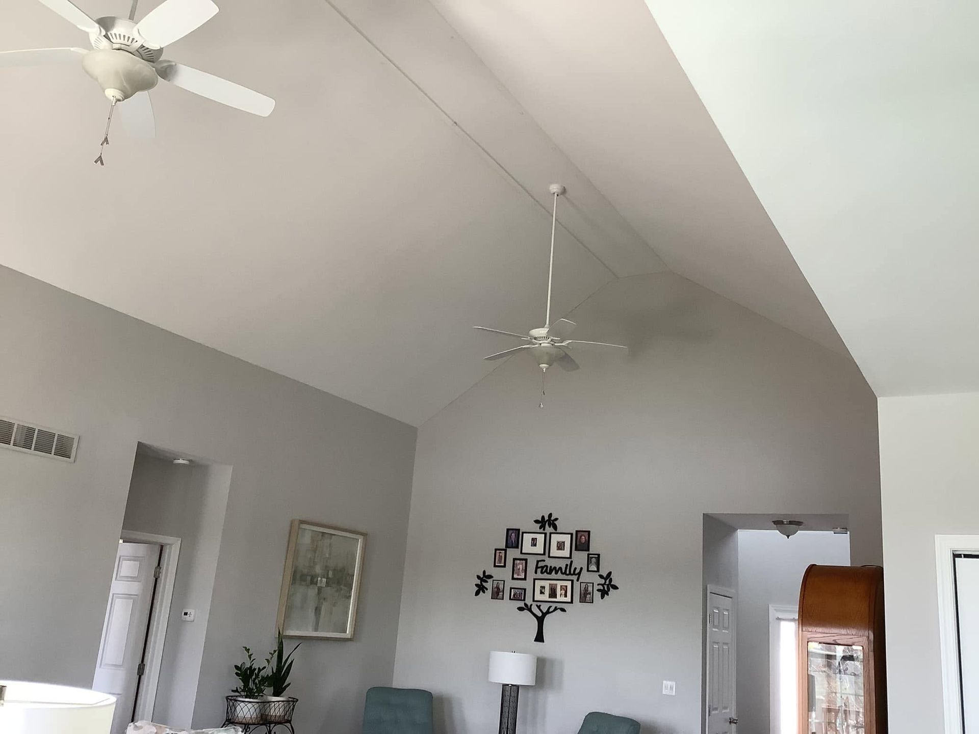 Bright living room with vaulted ceiling, white ceiling fans, gray walls, and wall decor