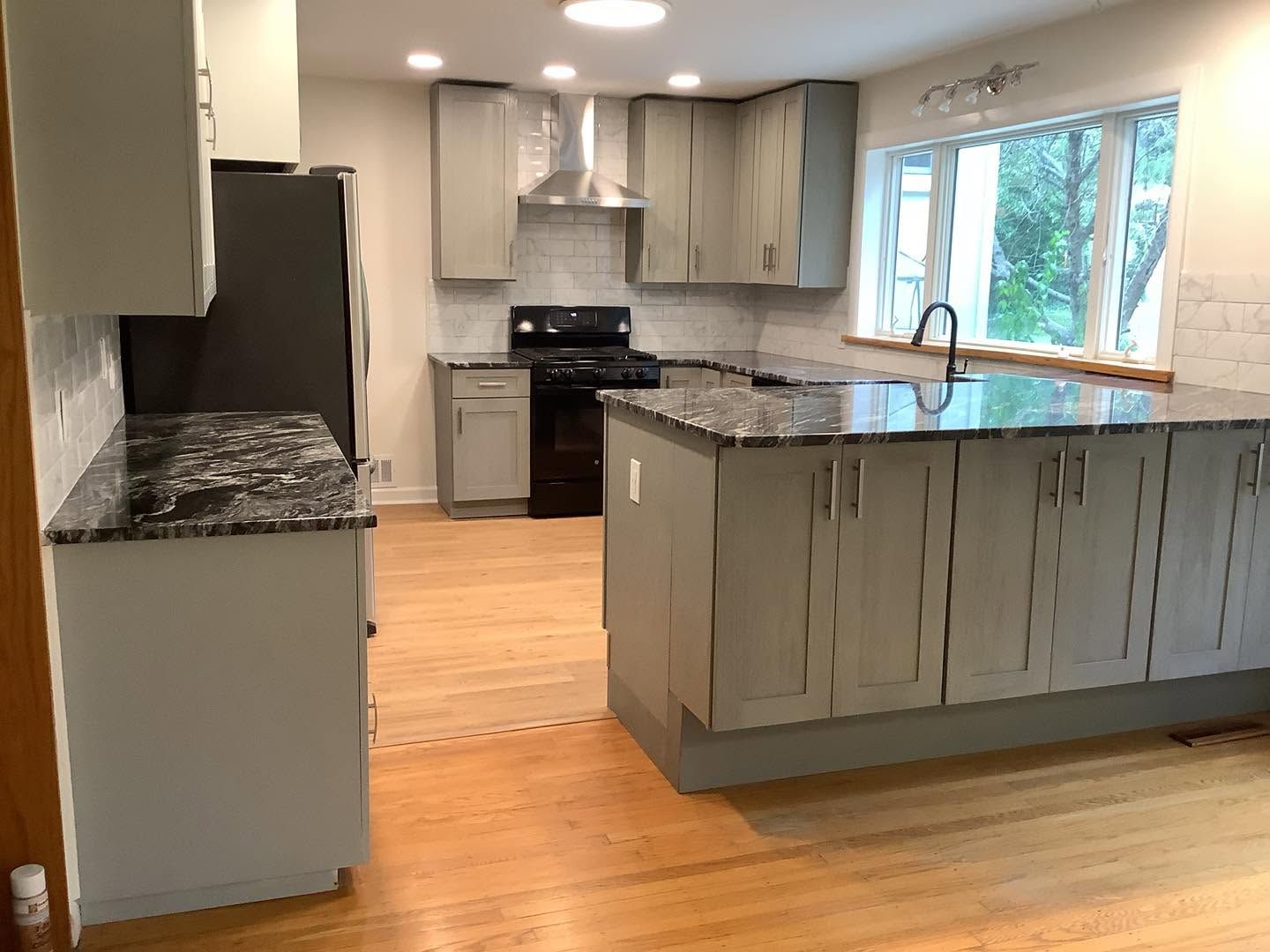 Modern kitchen with gray cabinets, granite counters, stainless appliances, and a central island by a window.