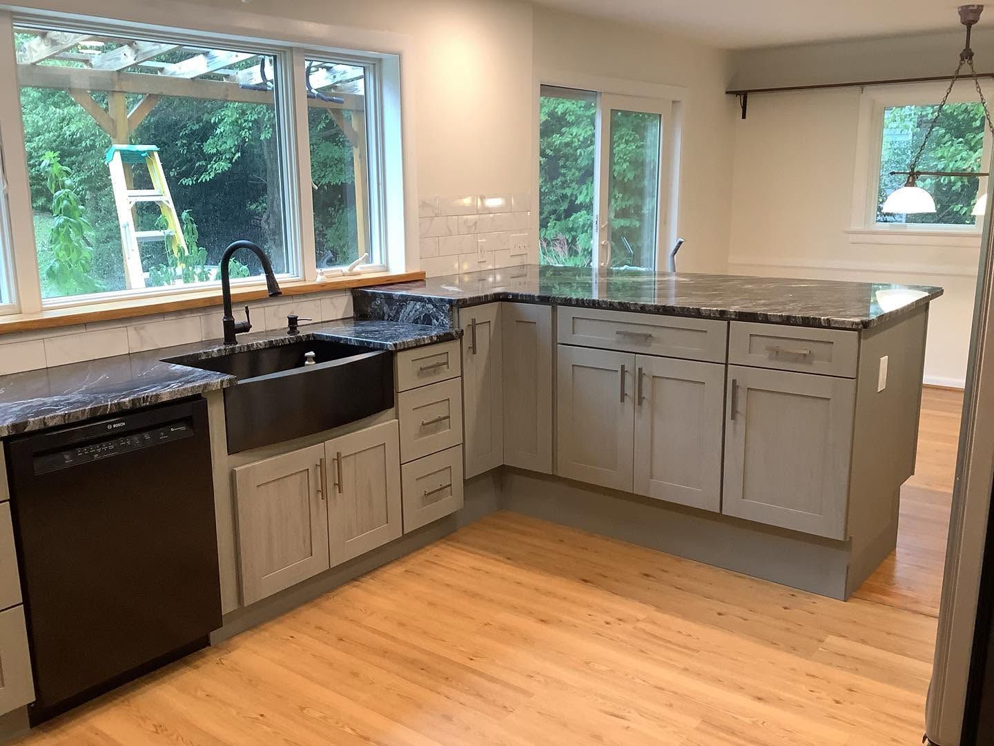 Modern kitchen with gray cabinets, black countertops, and large windows overlooking greenery