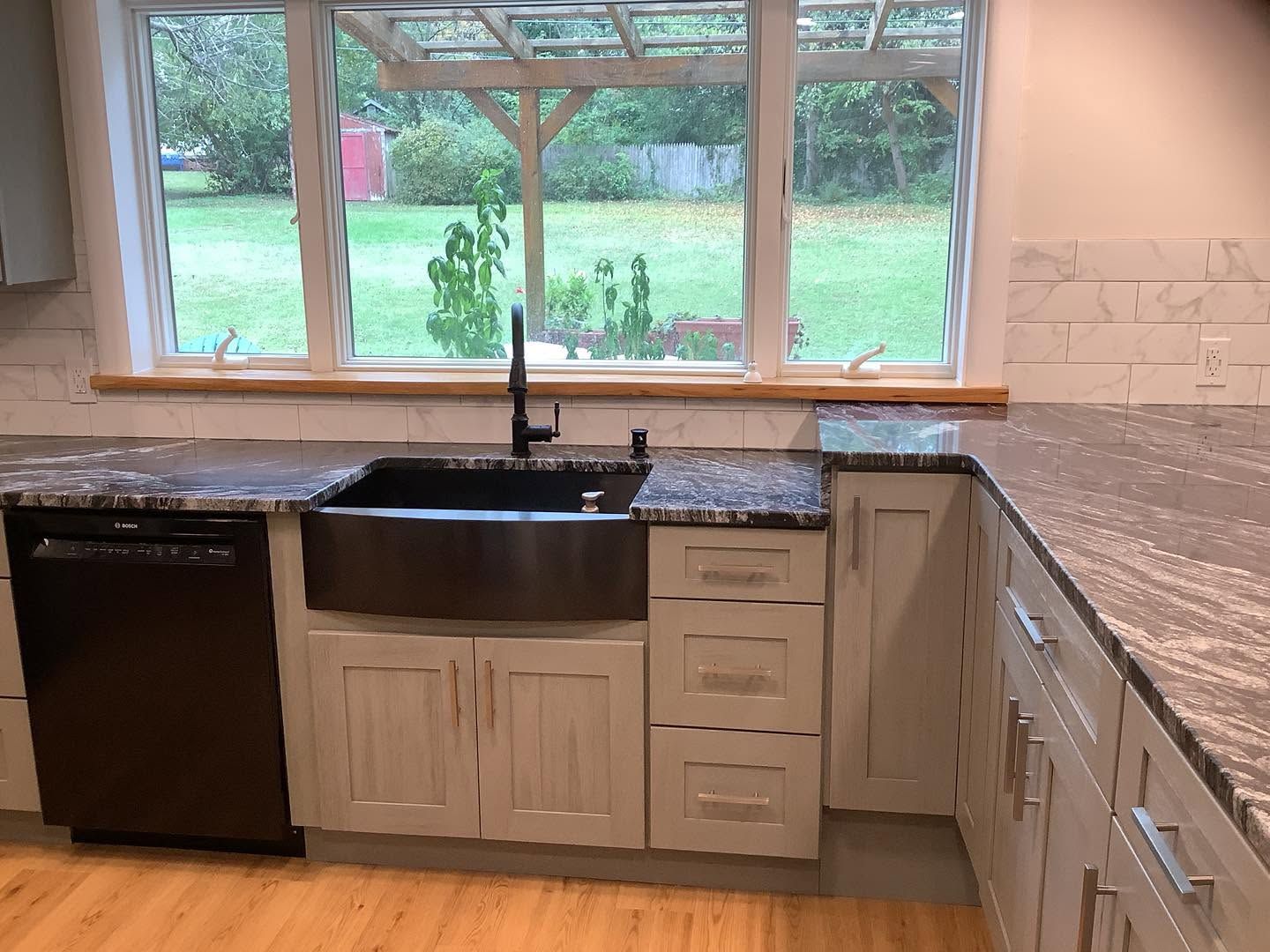 Kitchen with black sink under window, light cabinets, and speckled granite countertops.