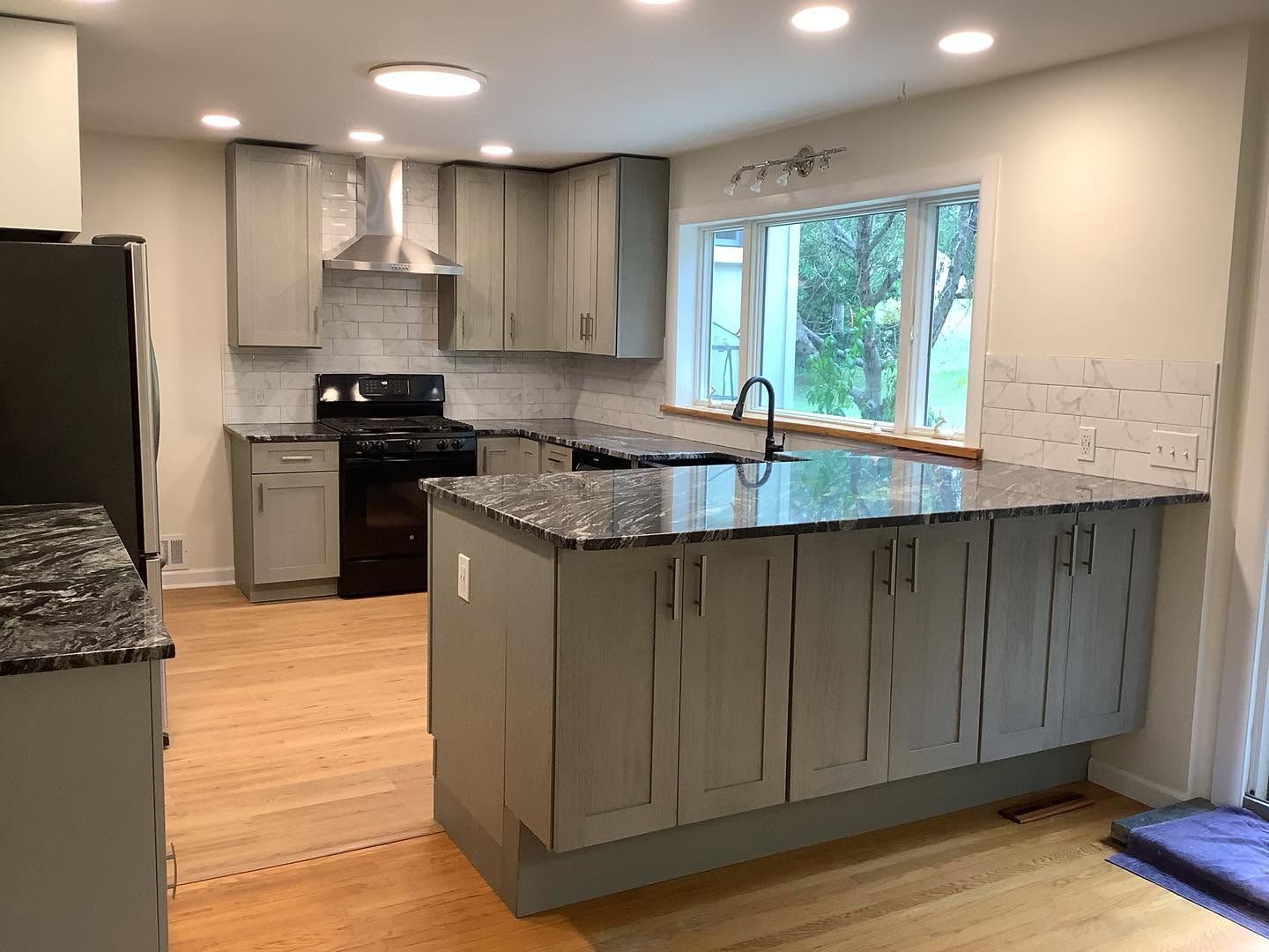 Modern kitchen with gray cabinets, granite island, stainless appliances, and large window over sink