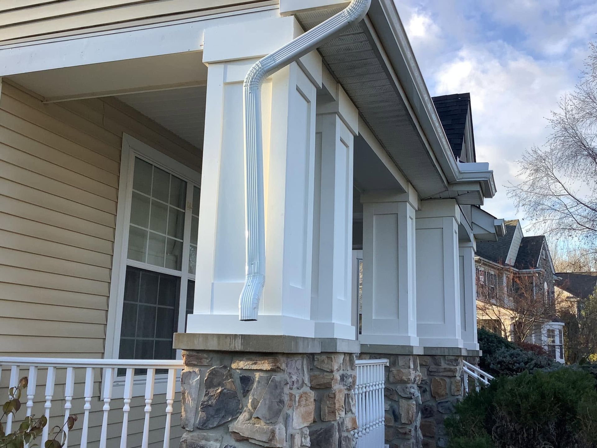 White porch column on a beige house with a stone base and railing, viewed from the front corner