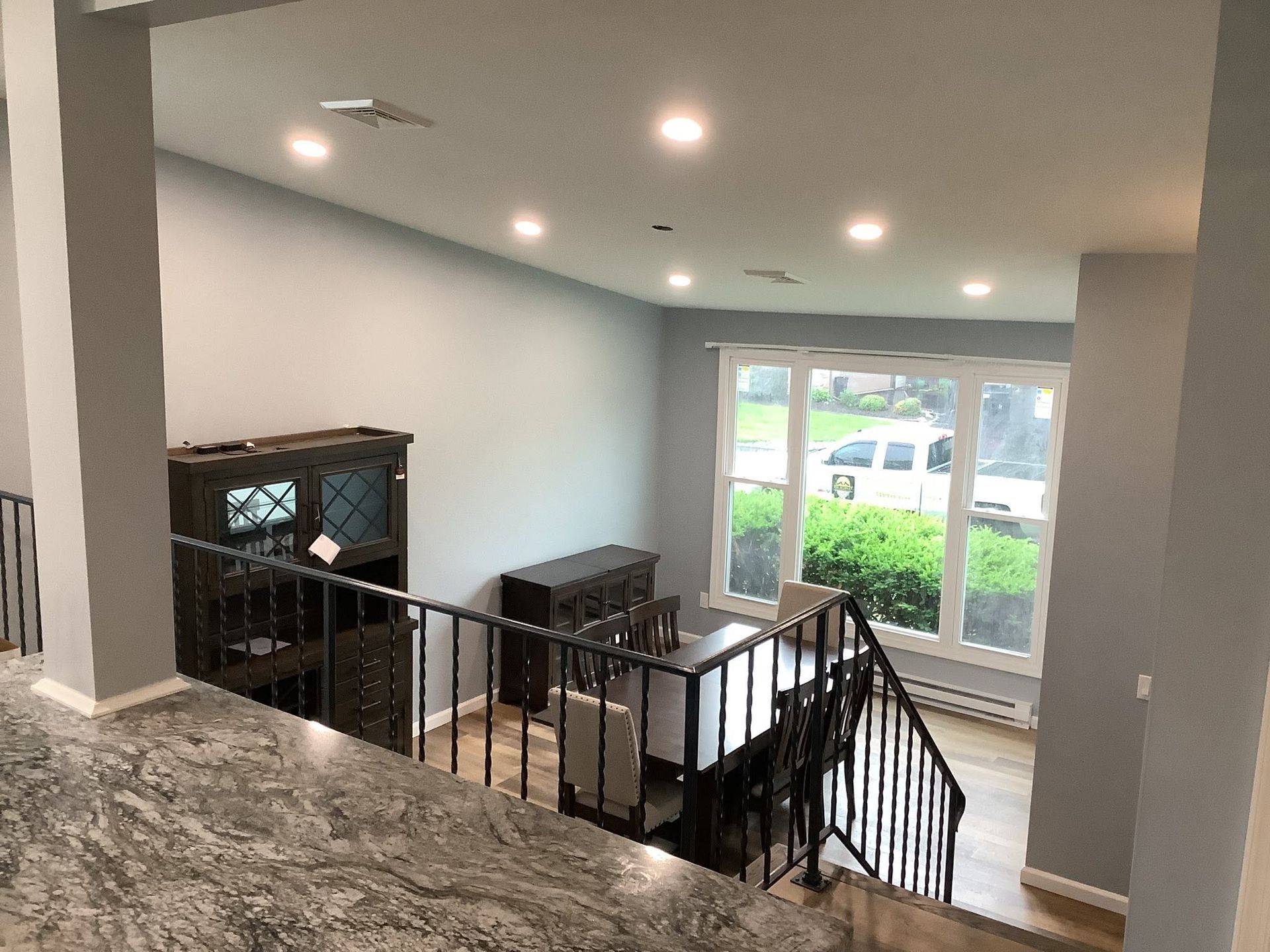 Modern home interior with carpeted stairs, black railing, gray walls, and large window overlooking greenery