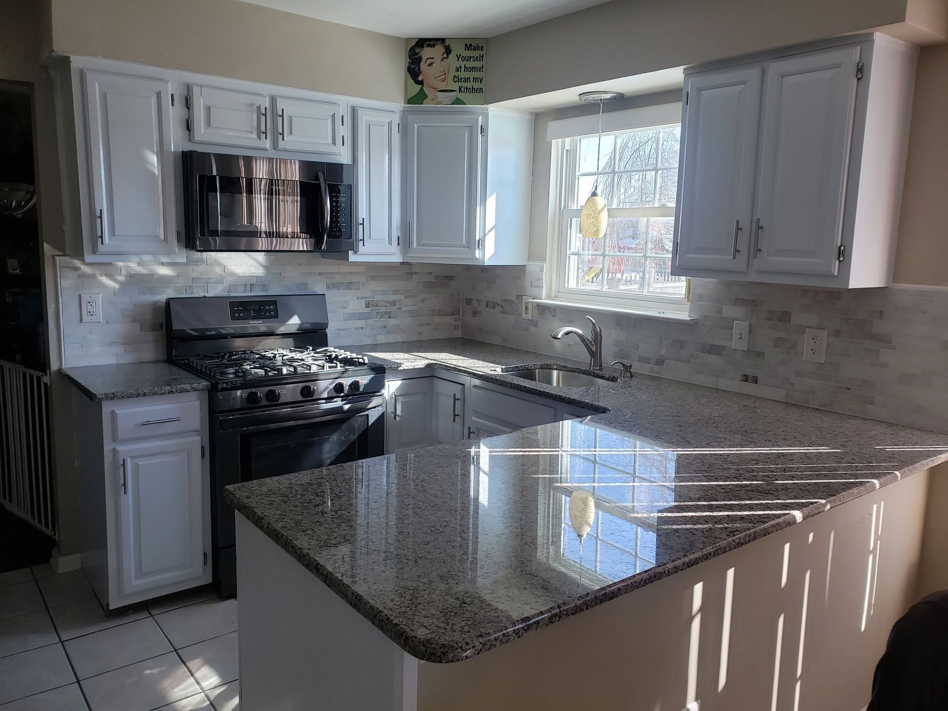Bright kitchen with white cabinets, granite island, black stove, and sunlit window above the sink