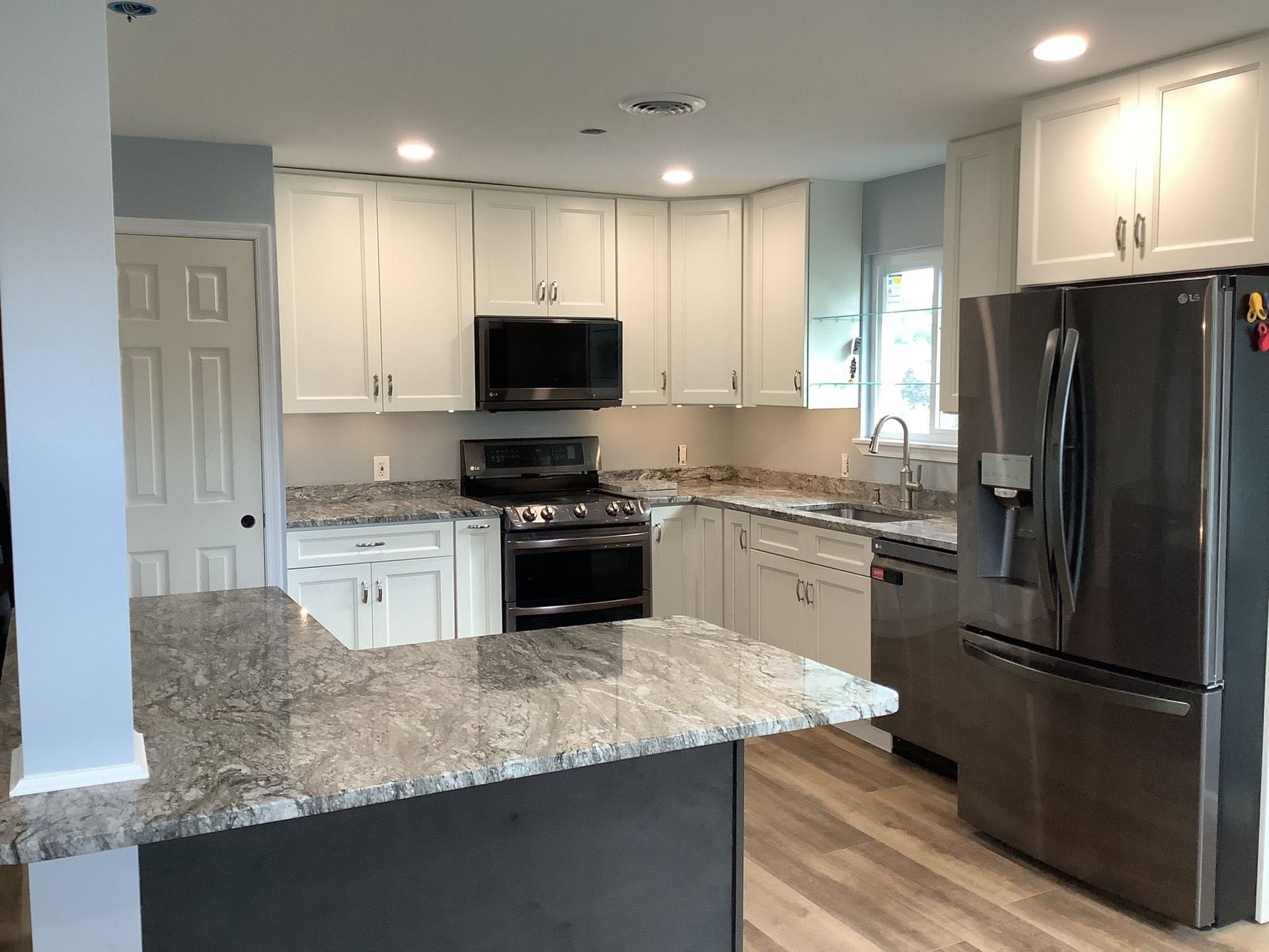 Modern kitchen with white cabinets, granite counters, stainless appliances, and dark refrigerator.