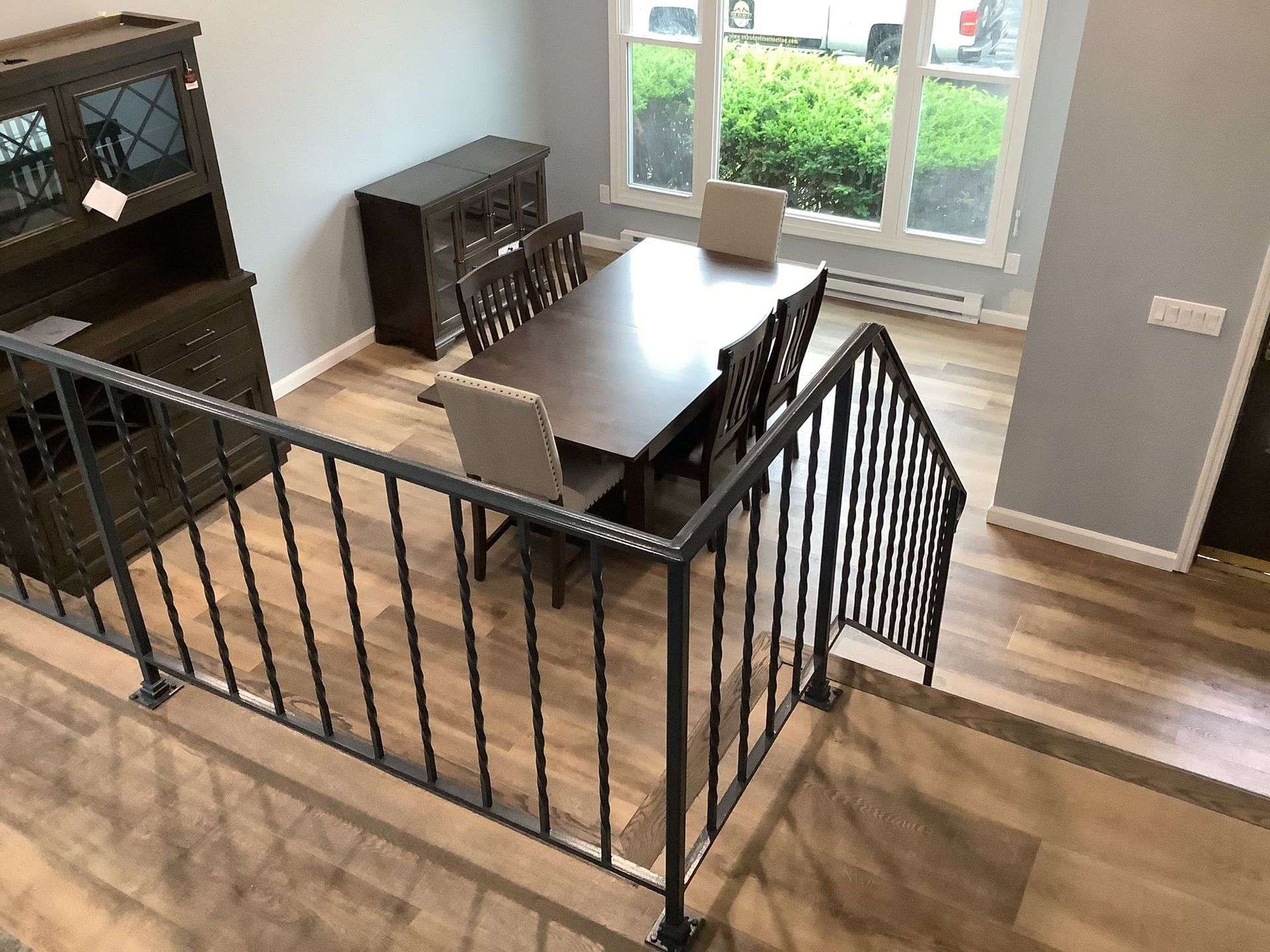 Dining room with dark wood table, chairs, and baby gate on hardwood floor near a window.