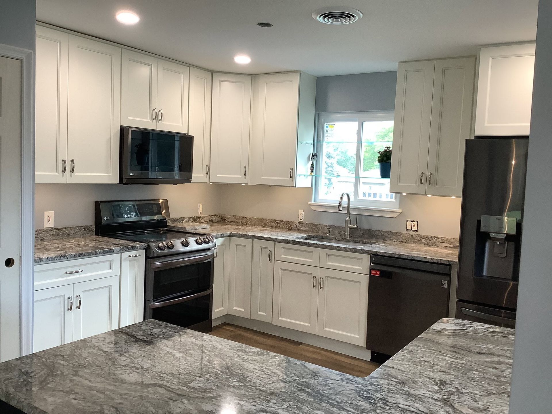 Bright modern kitchen with white cabinets, granite counters, black appliances, and a window over the sink