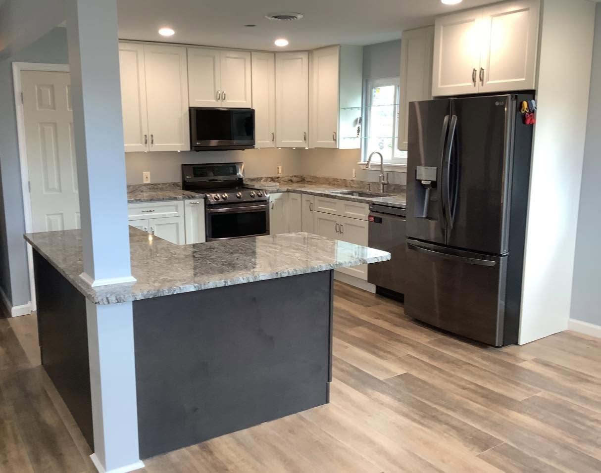 Modern kitchen with white cabinets, granite island, black appliances, and wood-look flooring