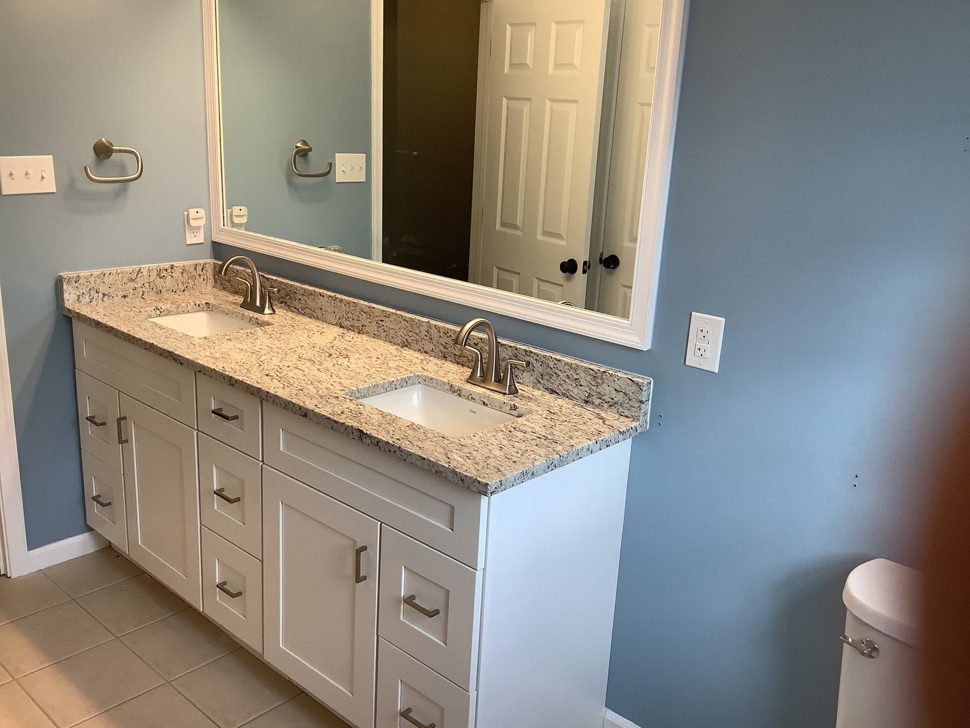Bathroom vanity with double sinks, granite countertop, and large mirror against blue walls.