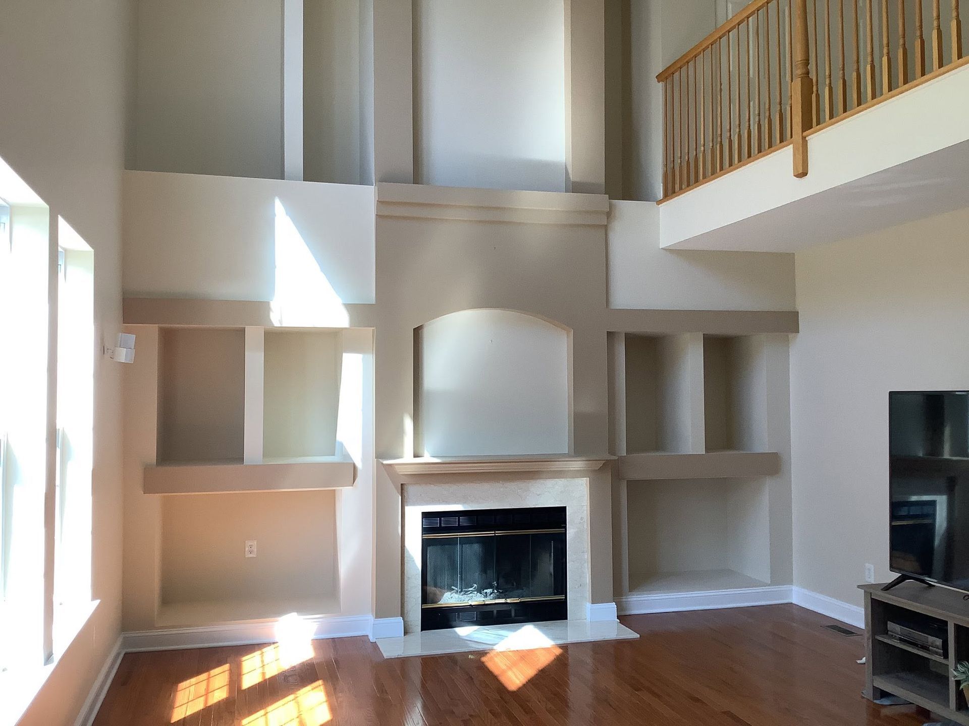 Bright living room with fireplace, built-in shelves, tall windows, and a loft balcony above