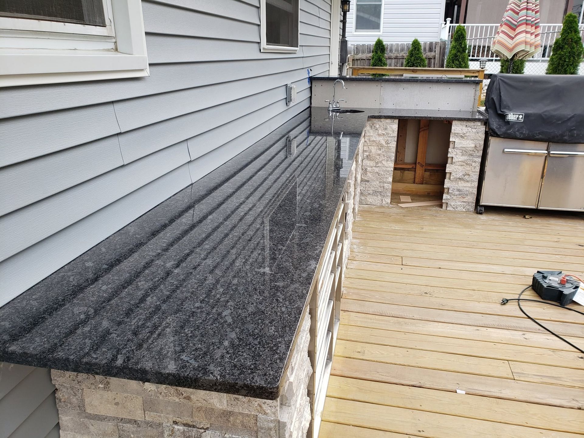 Gray house siding beside a black shingled roof and wooden deck under construction