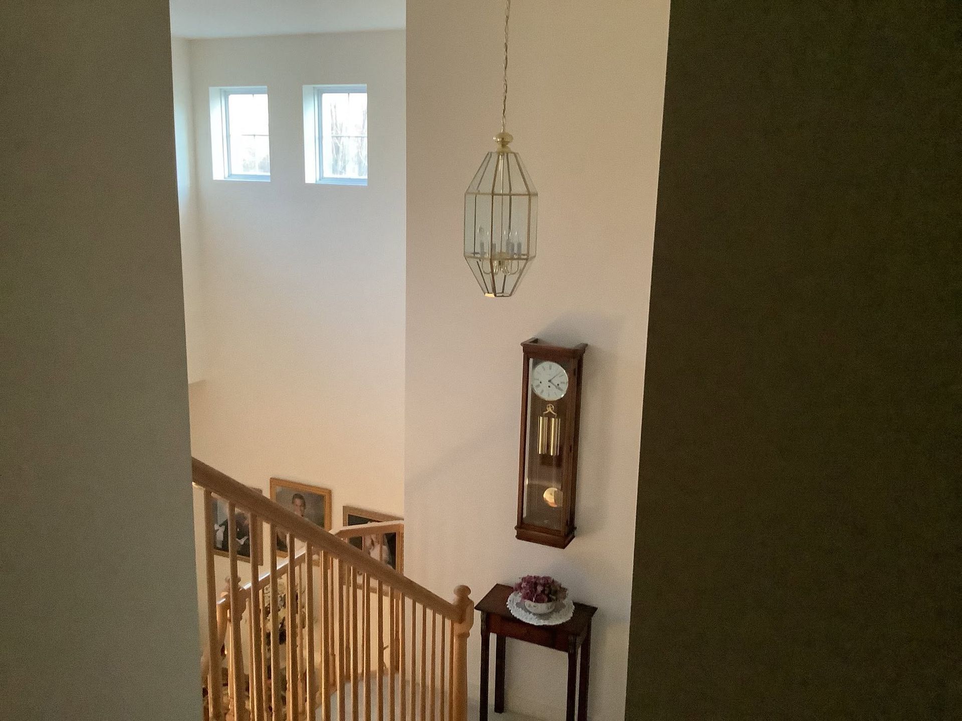 Staircase landing with wall clock, hanging light, and two small windows on a white wall.