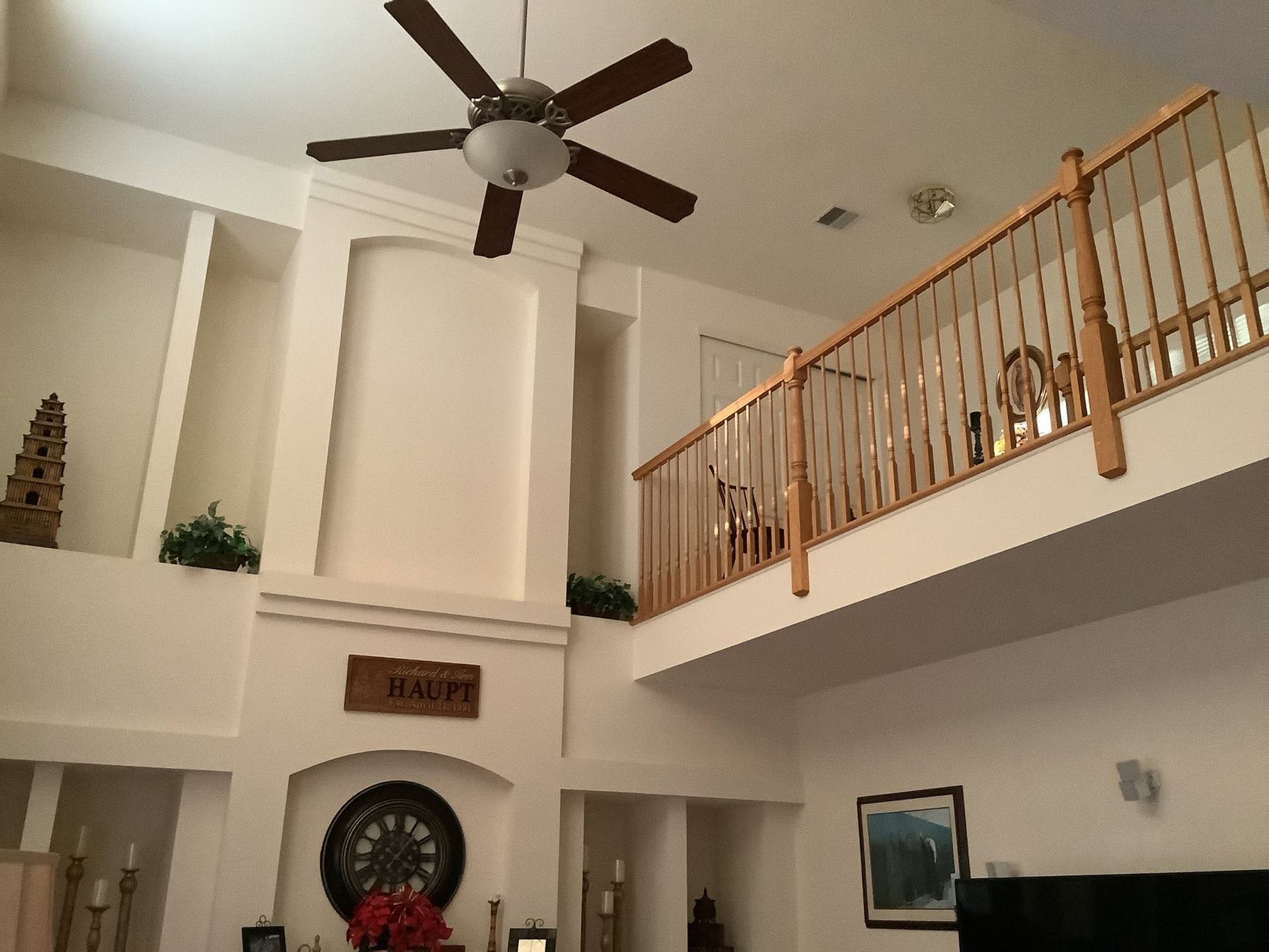 Bright living room with vaulted ceiling, ceiling fan, staircase railing, and wall decor